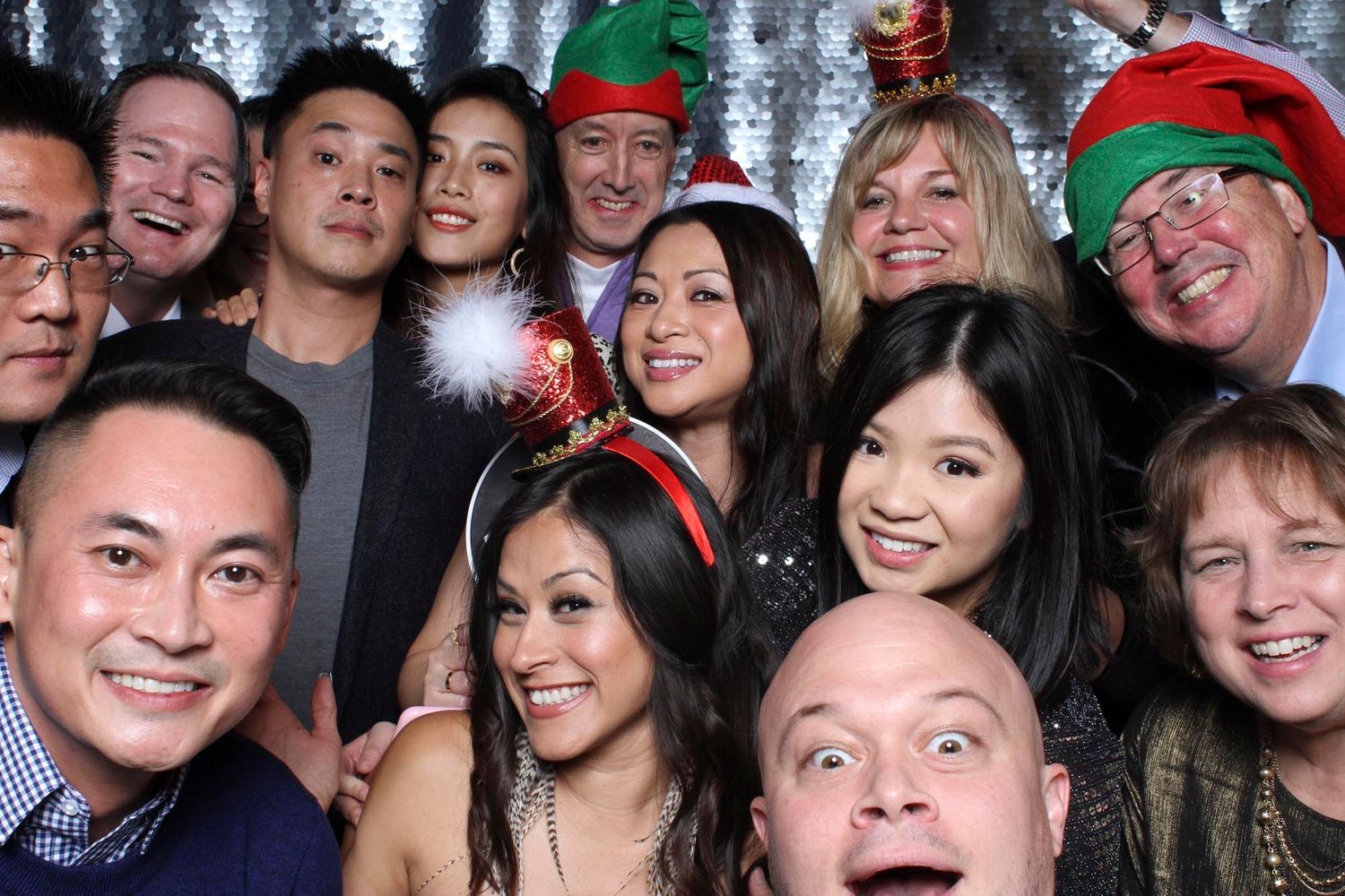 Group of friends posing at a festive Christmas party photo booth, wearing holiday hats and accessories.