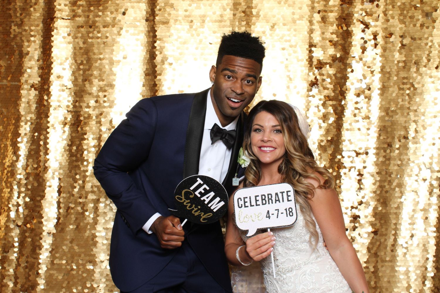 Couple posing with celebrate signs at a gold sequin wedding photo booth on April 7, 2018.
