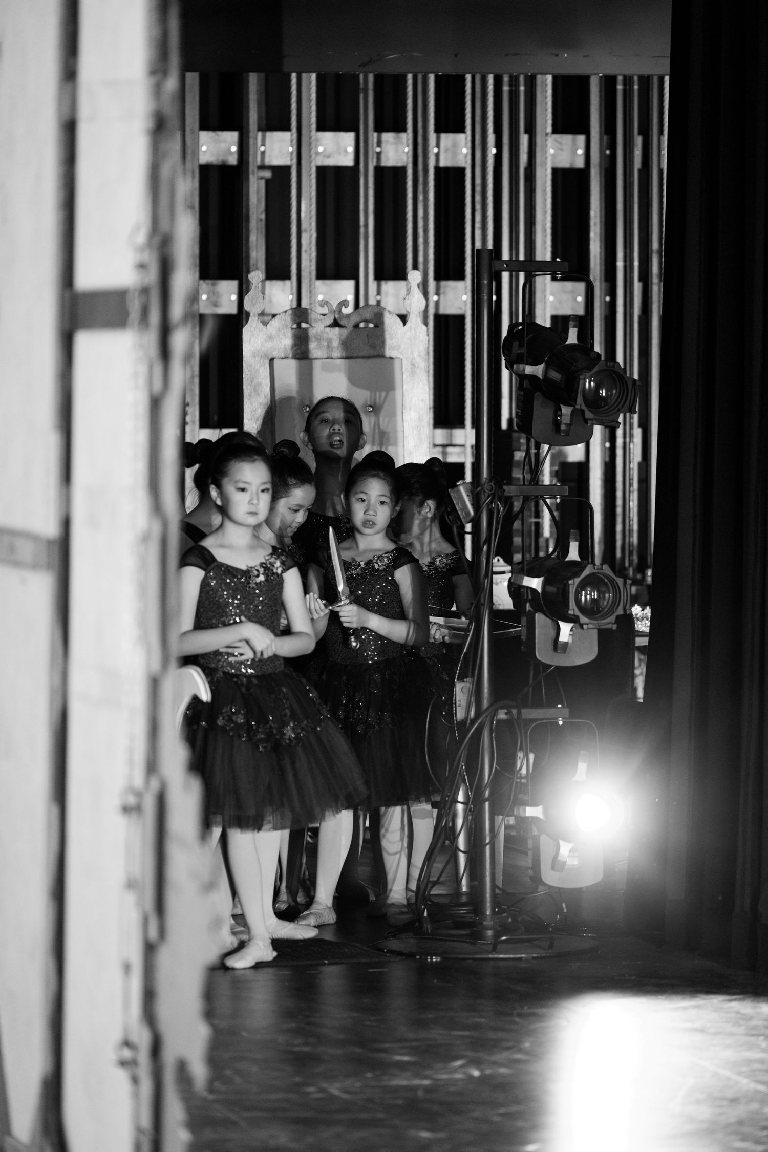 Young ballet dancers in black tutus wait backstage near stage lights before a performance. Las Positas College