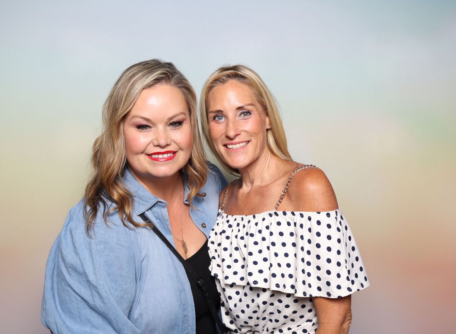 Two smiling women posing together in front of a pastel rainbow background at a photo booth event  at the Shine in Pleasanton.