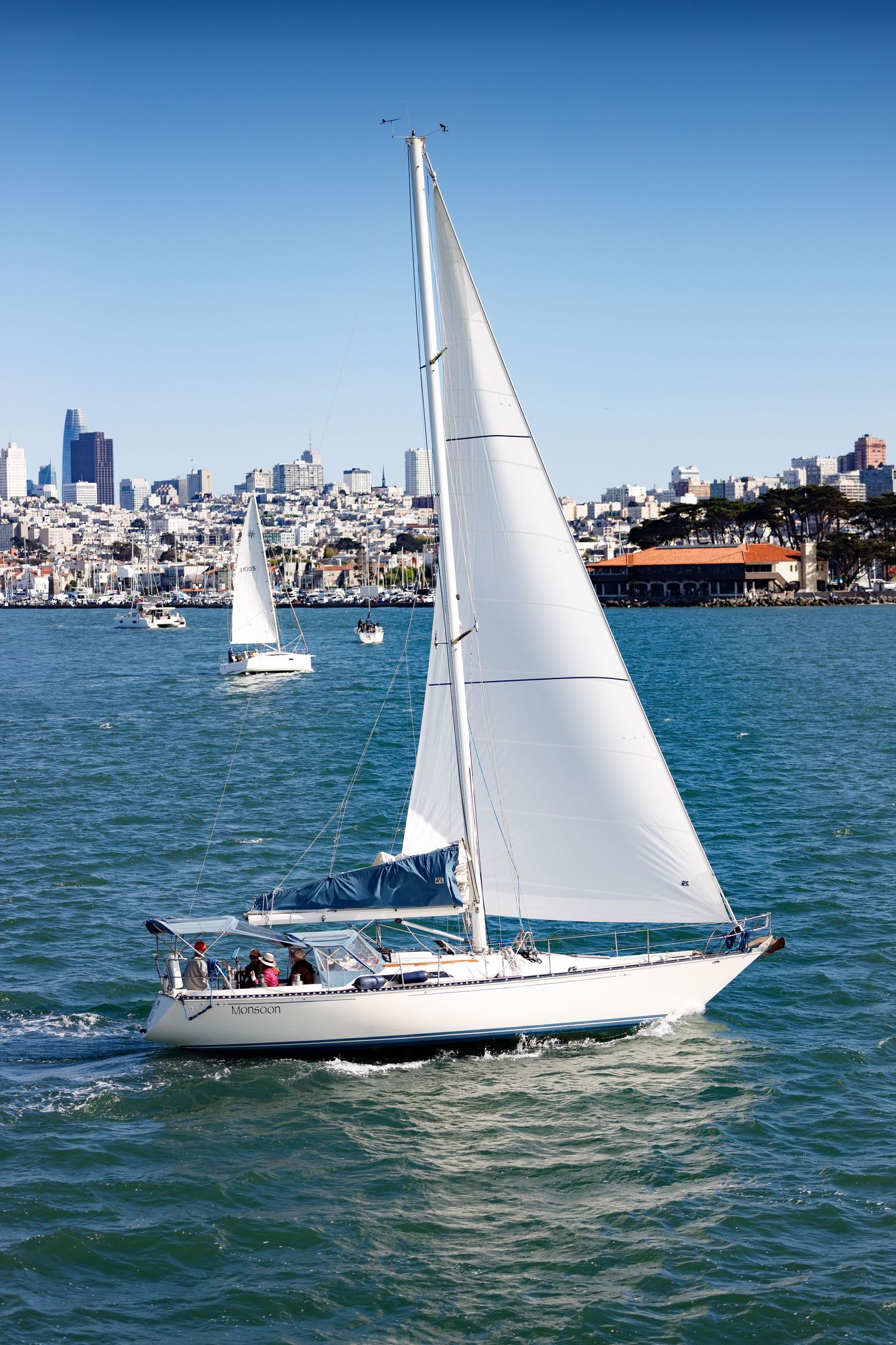 Sailboat gliding through San Francisco Bay with the city skyline and clear blue skies in the background.