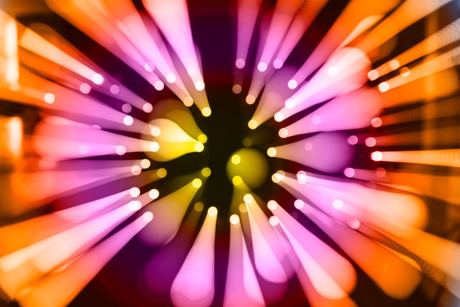 Abstract burst of glowing pink, orange, and yellow light rays radiating from a dark center on a bokeh background.