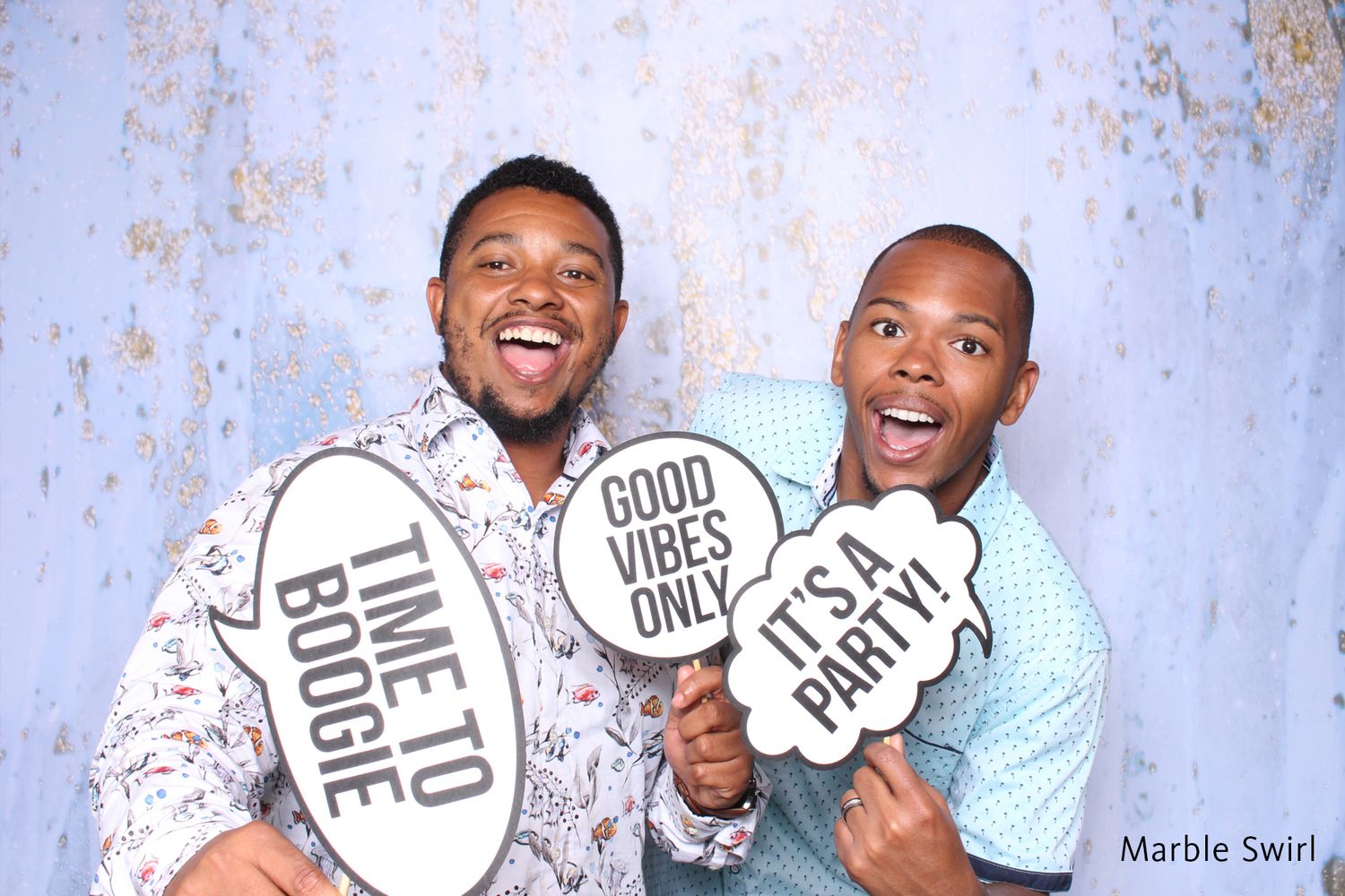 Two men laughing and holding fun photo booth signs with Good Vibes Only and Time to Boogie.