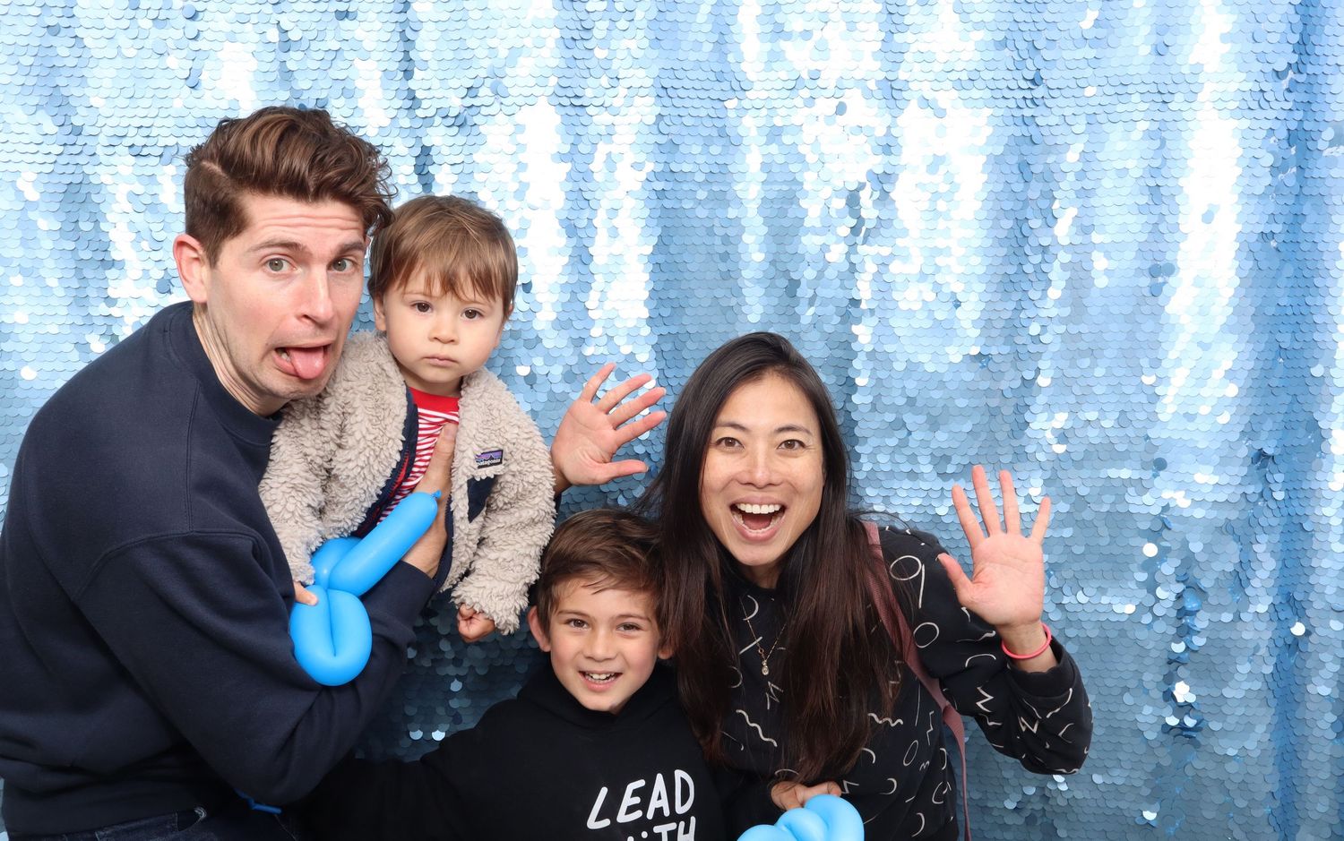 Family of four posing happily in front of a blue sequin backdrop at a Pacific Primary block party in San Francisco.