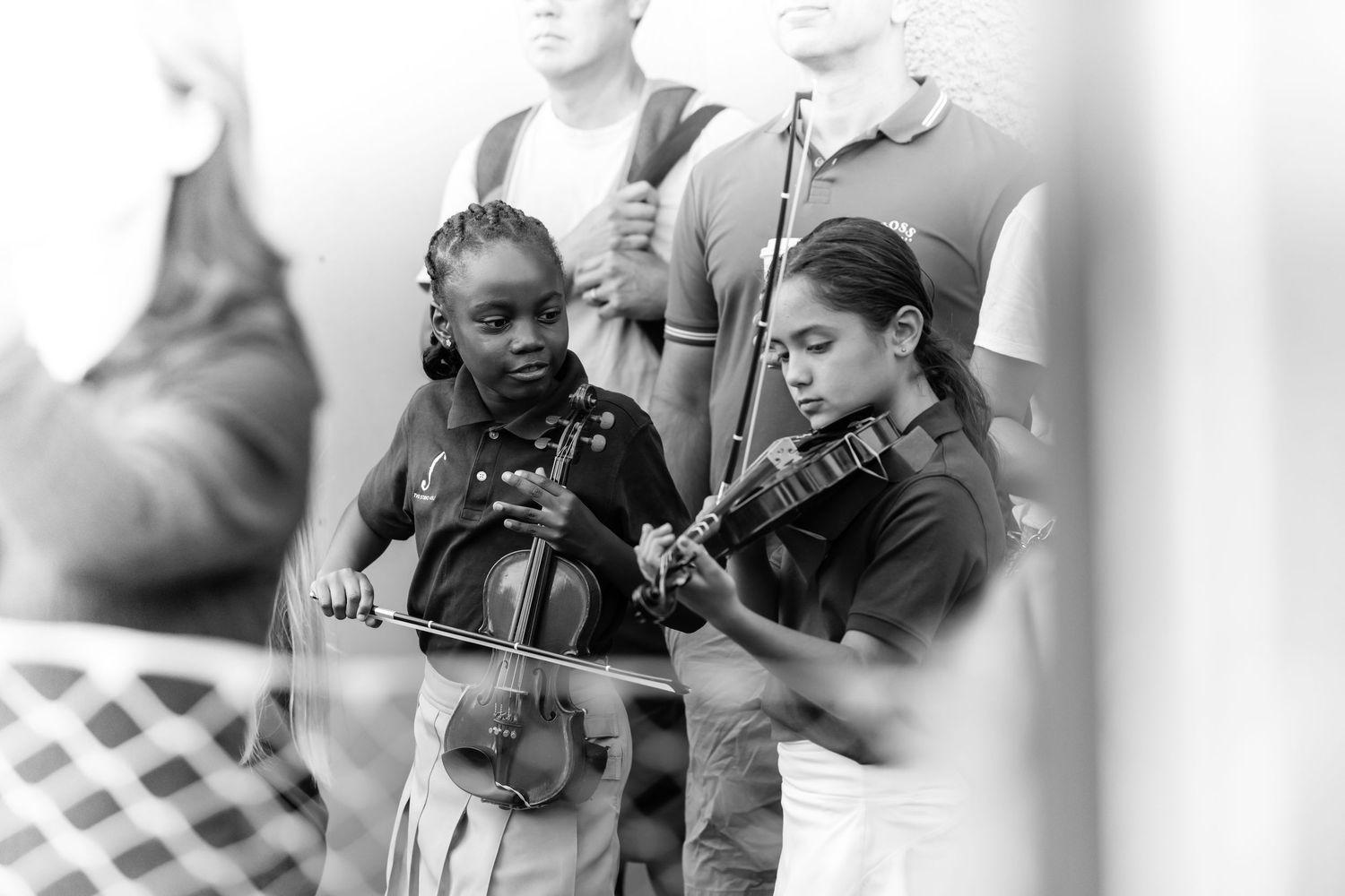 Two young girls playing violins outdoors in a black and white photo at a music event.
