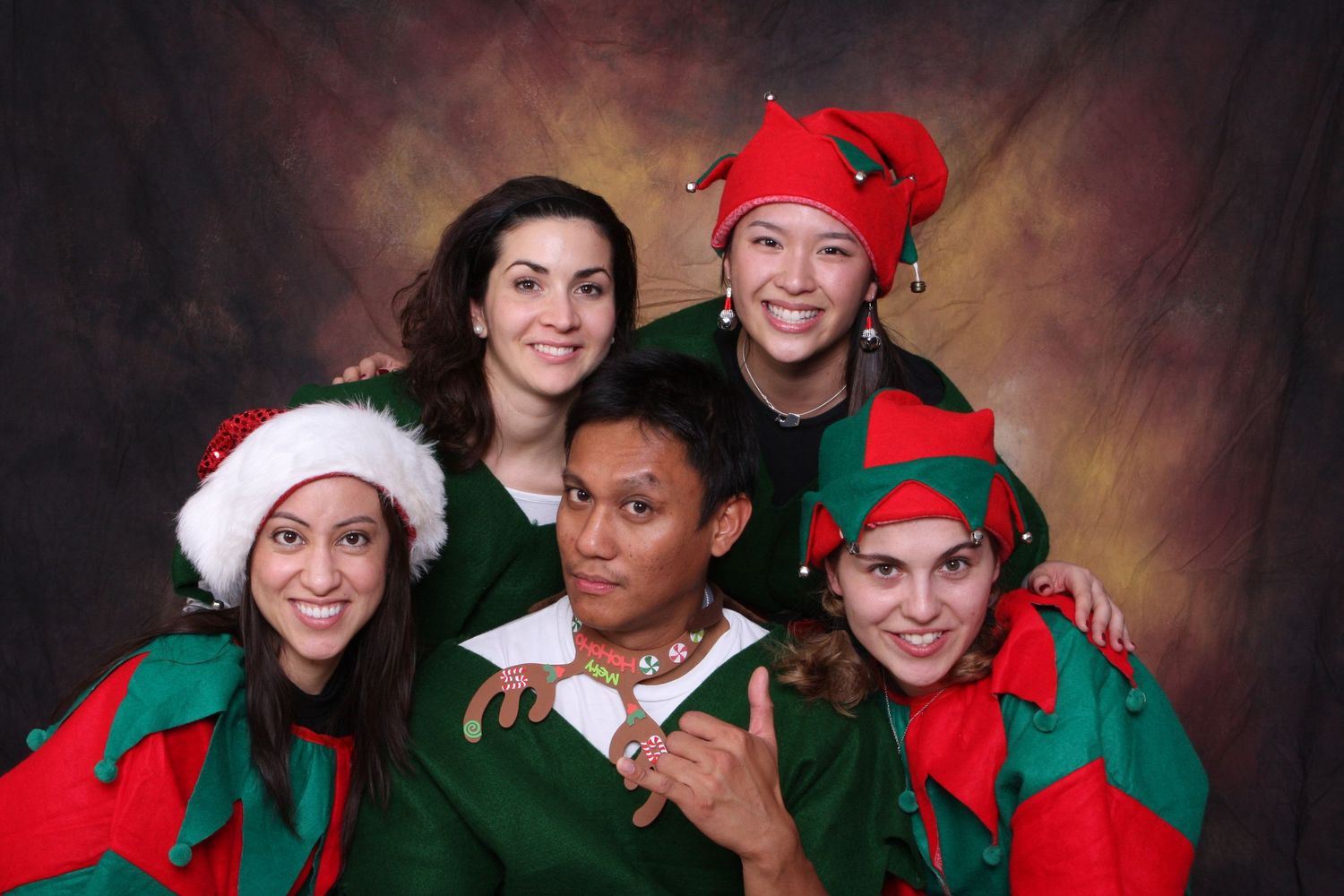 Five people in festive Christmas elf costumes pose together smiling for a holiday group photo. Gensler Holiday Party