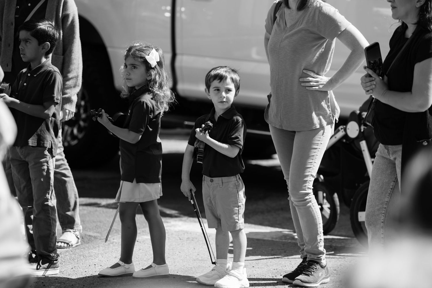 Black and white photo of young children standing outdoors at a community event with adults nearby.