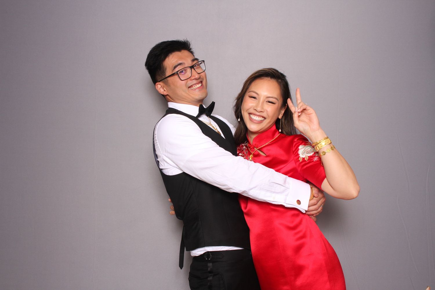 Couple posing playfully in photo booth, man in vest and woman in red cheongsam making peace sign. Reception in Pearl Bay Restaurant Fremont