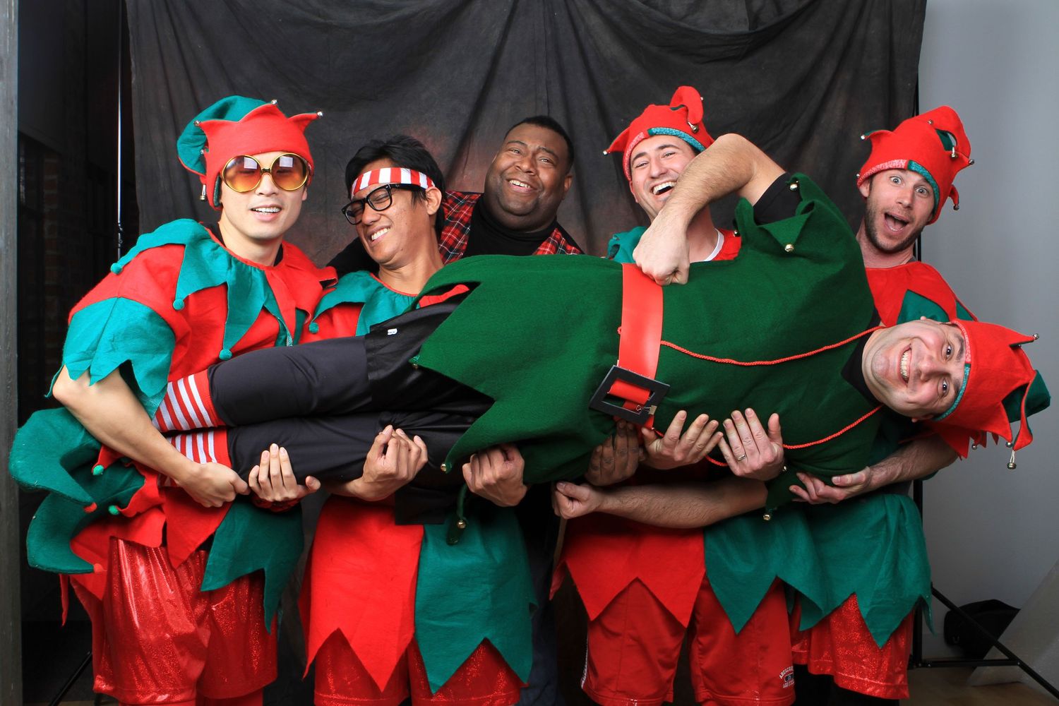 Group of six people dressed in festive red and green elf costumes posing playfully for a holiday photo. Gensler Holiday Party