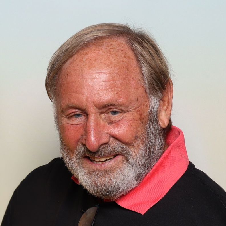 Elderly man smiling, wearing a black jacket with pink collar outdoors - Bob Rossi owner of the Saloon in Pleasanton.