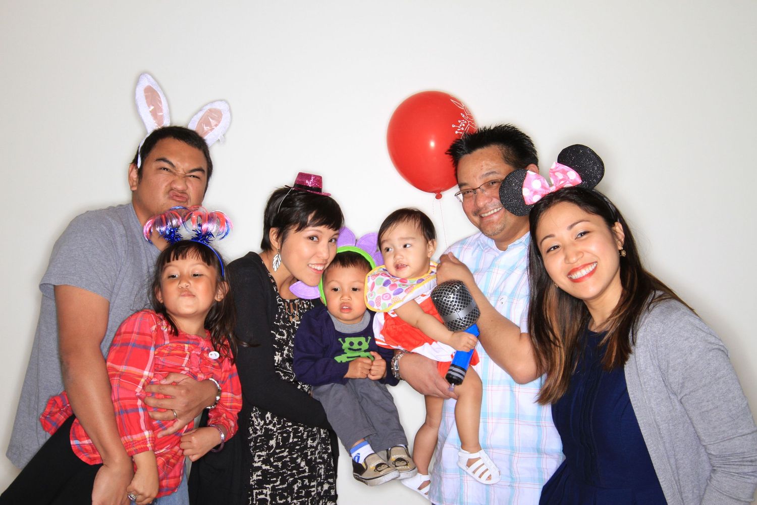 Family of seven posing with bunny ears, Mickey Mouse ears, and a red balloon at a festive party photo booth.