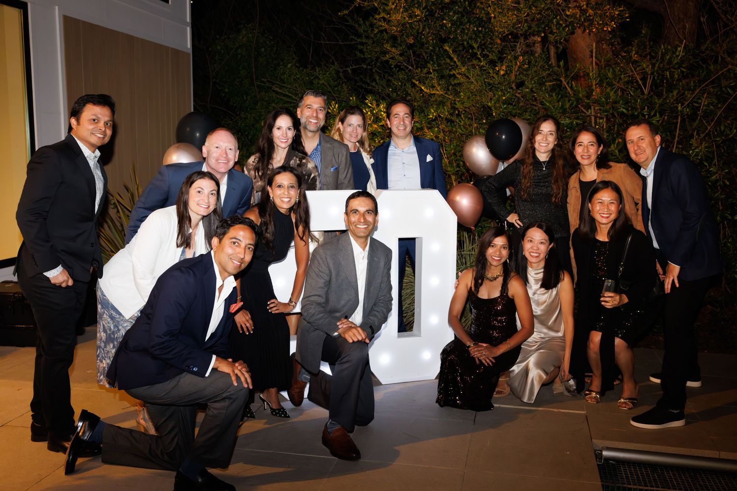 Group of professionals posing together at an elegant evening event beside illuminated decorative letters at an outdoor venue.