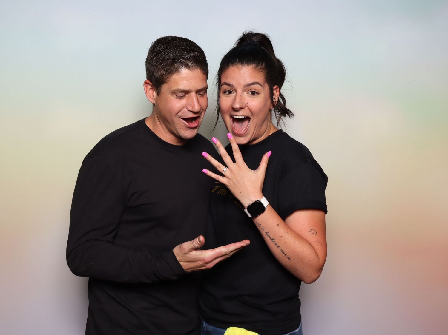 Excited couple in black shirts with colorful pastel background at the Shine in Pleasanton.