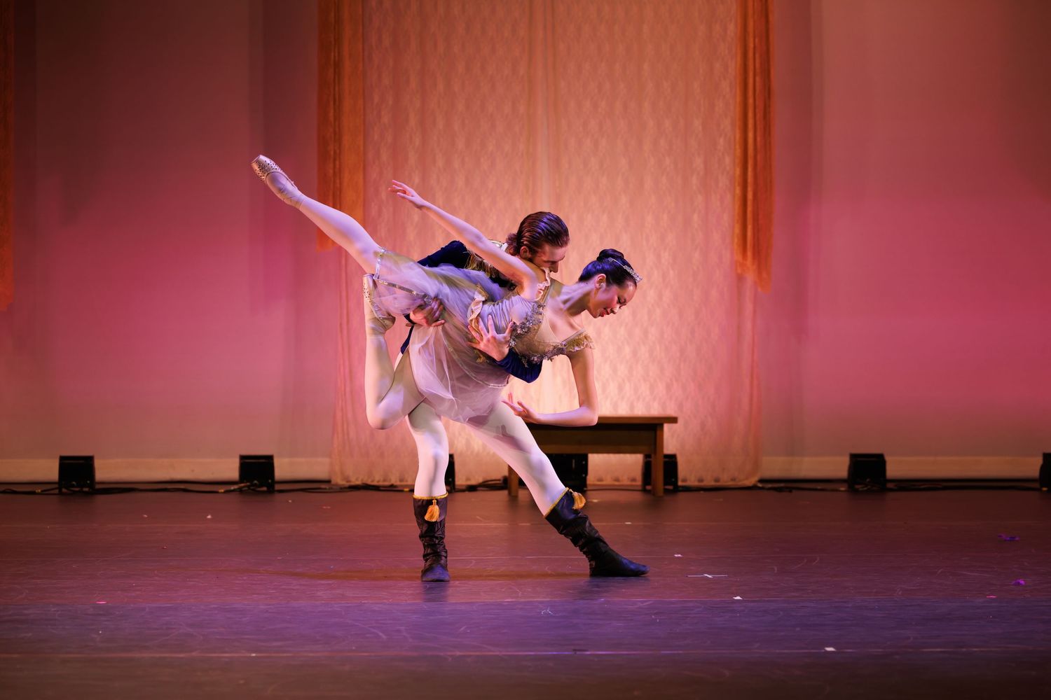 Two ballet dancers perform an elegant lift on stage, with warm pink lighting illuminating their graceful performance.  Las Positas College