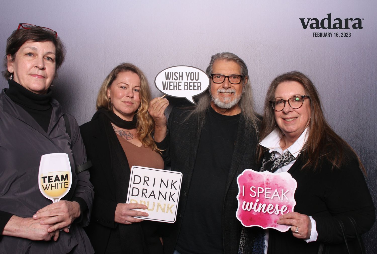Four adults pose with fun wine-themed props at a Vadara event in Alameda.
