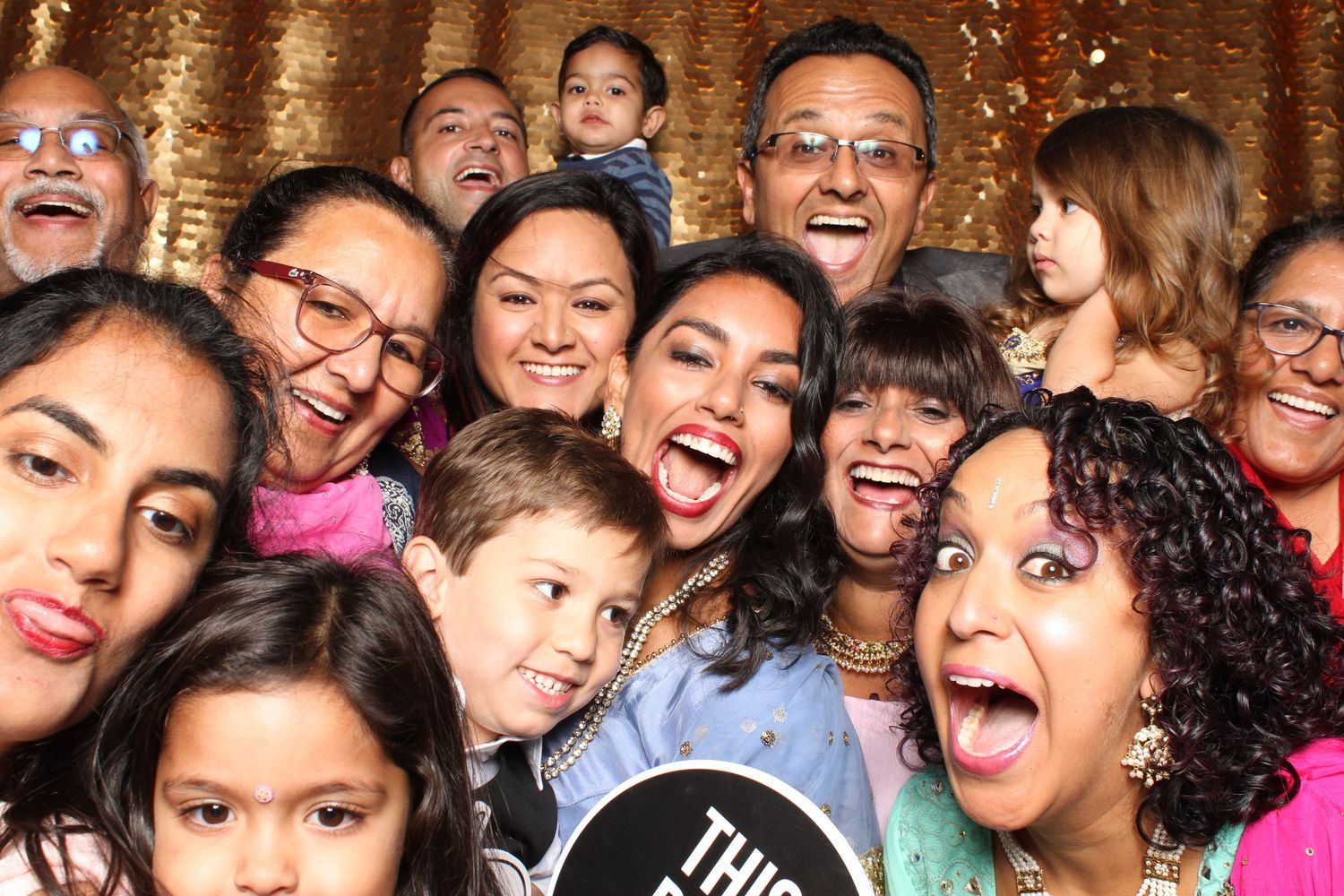 Large joyful family group photo at festive event with gold sequin backdrop.