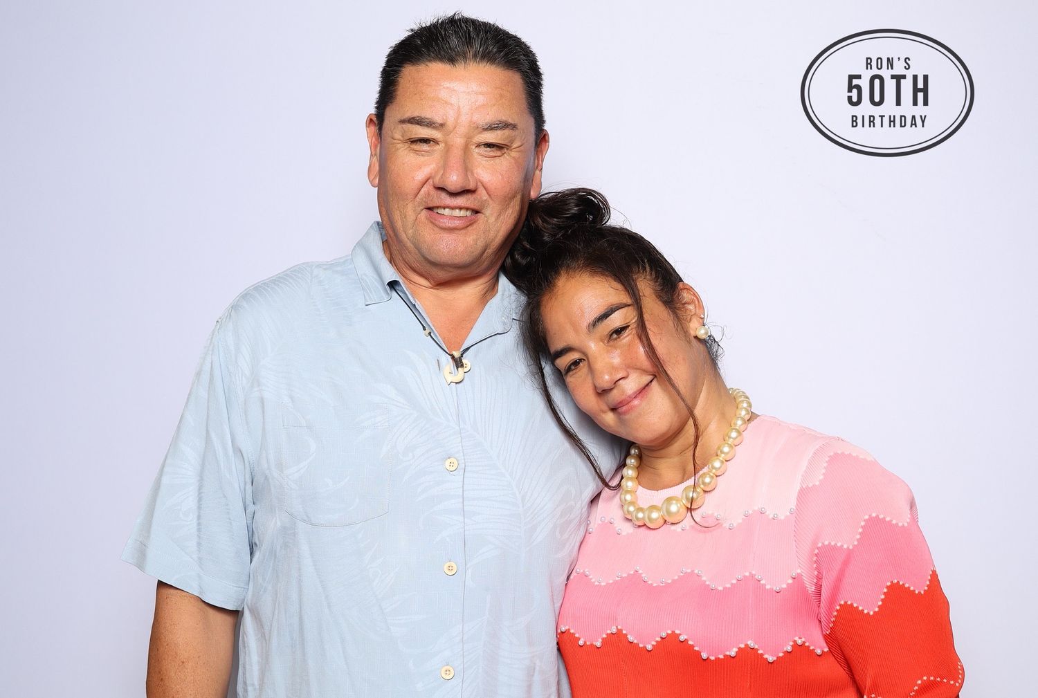 Two people smiling together at a 50th birthday celebration photo booth against a white background. Industrious, Walnut Creek.