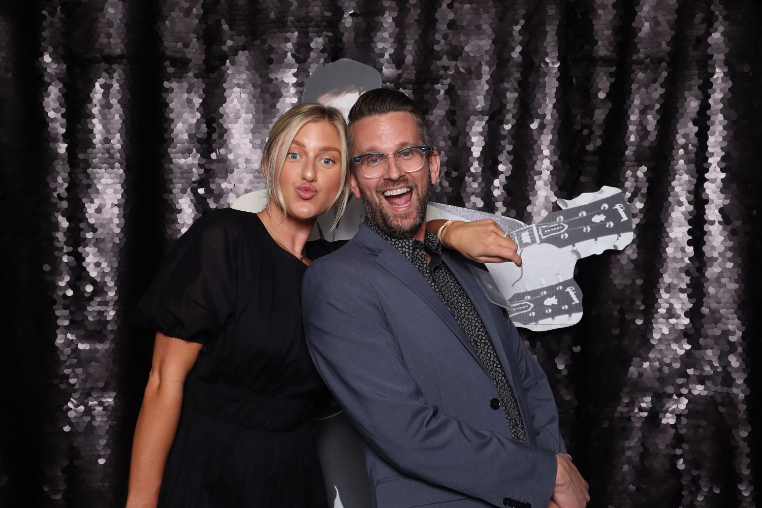 A man and woman pose playfully in front of a sequin backdrop at a photo booth event.