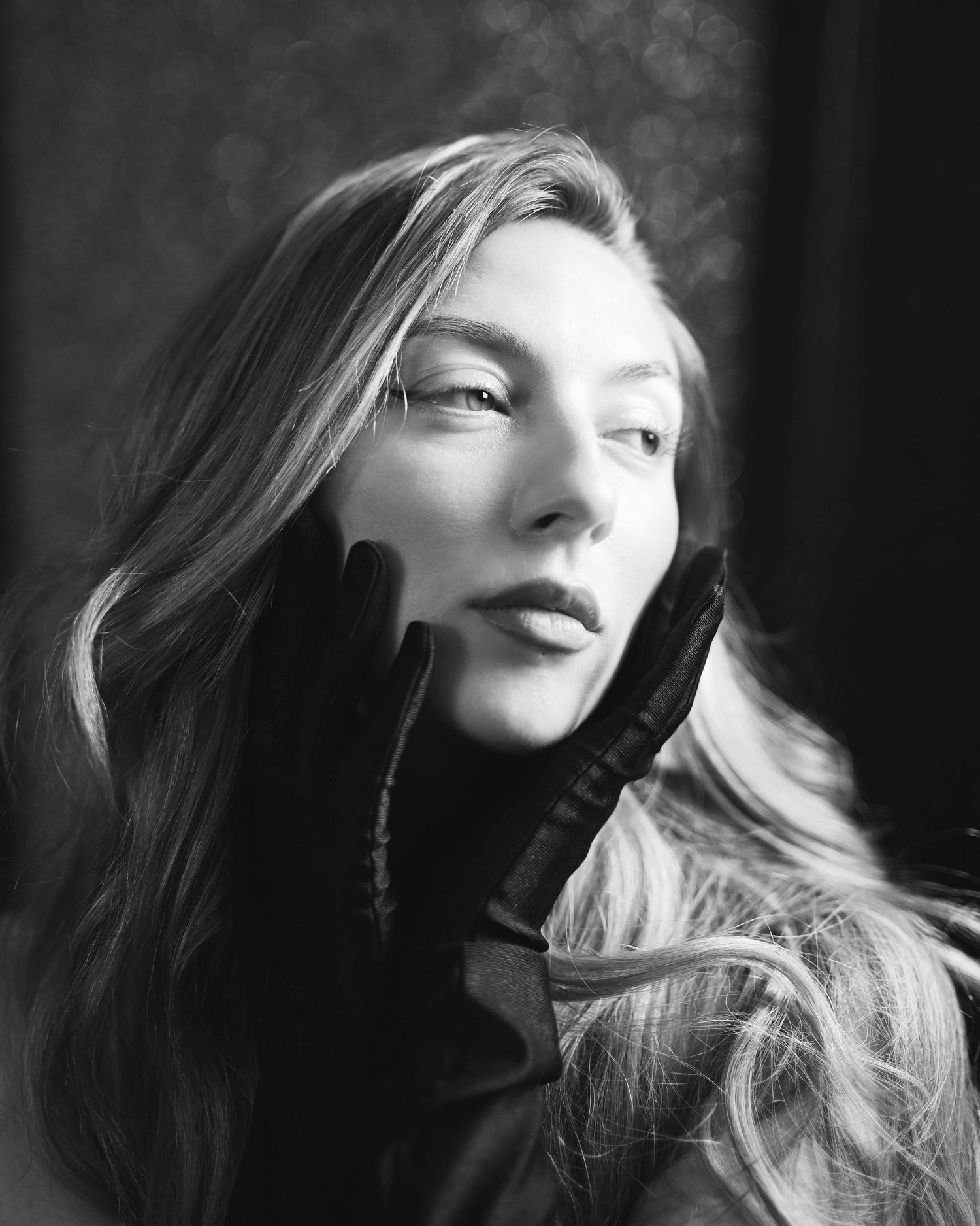 Black and white portrait of a young woman wearing black gloves, posing elegantly with her hands framing her face.