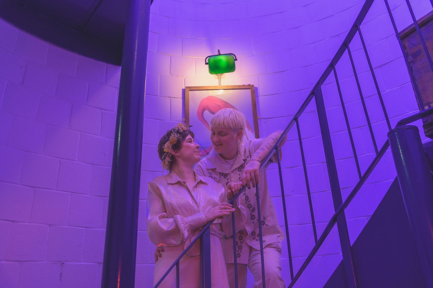 Two people standing close together in a purple-lit stairwell.