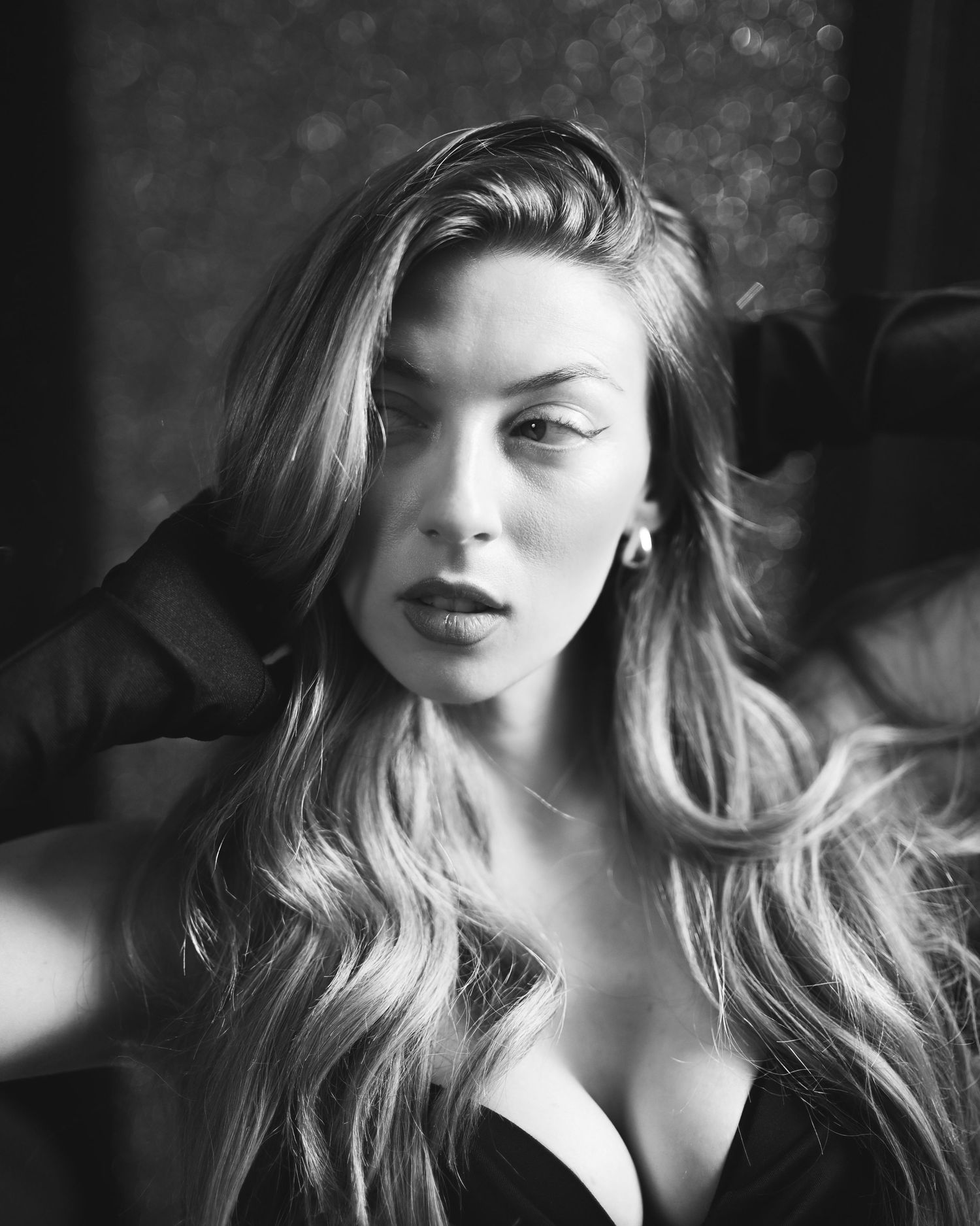 Black and white portrait of a young woman with long wavy blonde hair wearing a black top, posing elegantly.