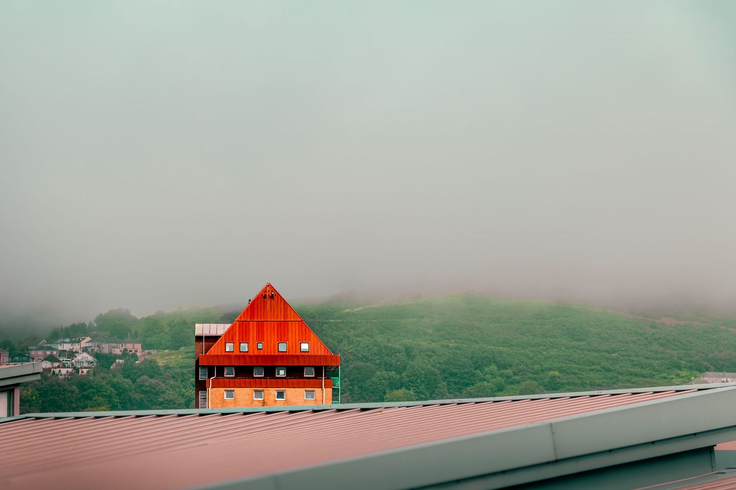 A red-roofed house sits against a misty green hillside on a foggy day.
