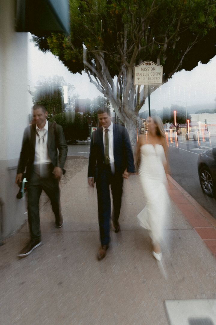 Blurred motion shot of wedding party walking on sidewalk near Mission San Luis Obispo.