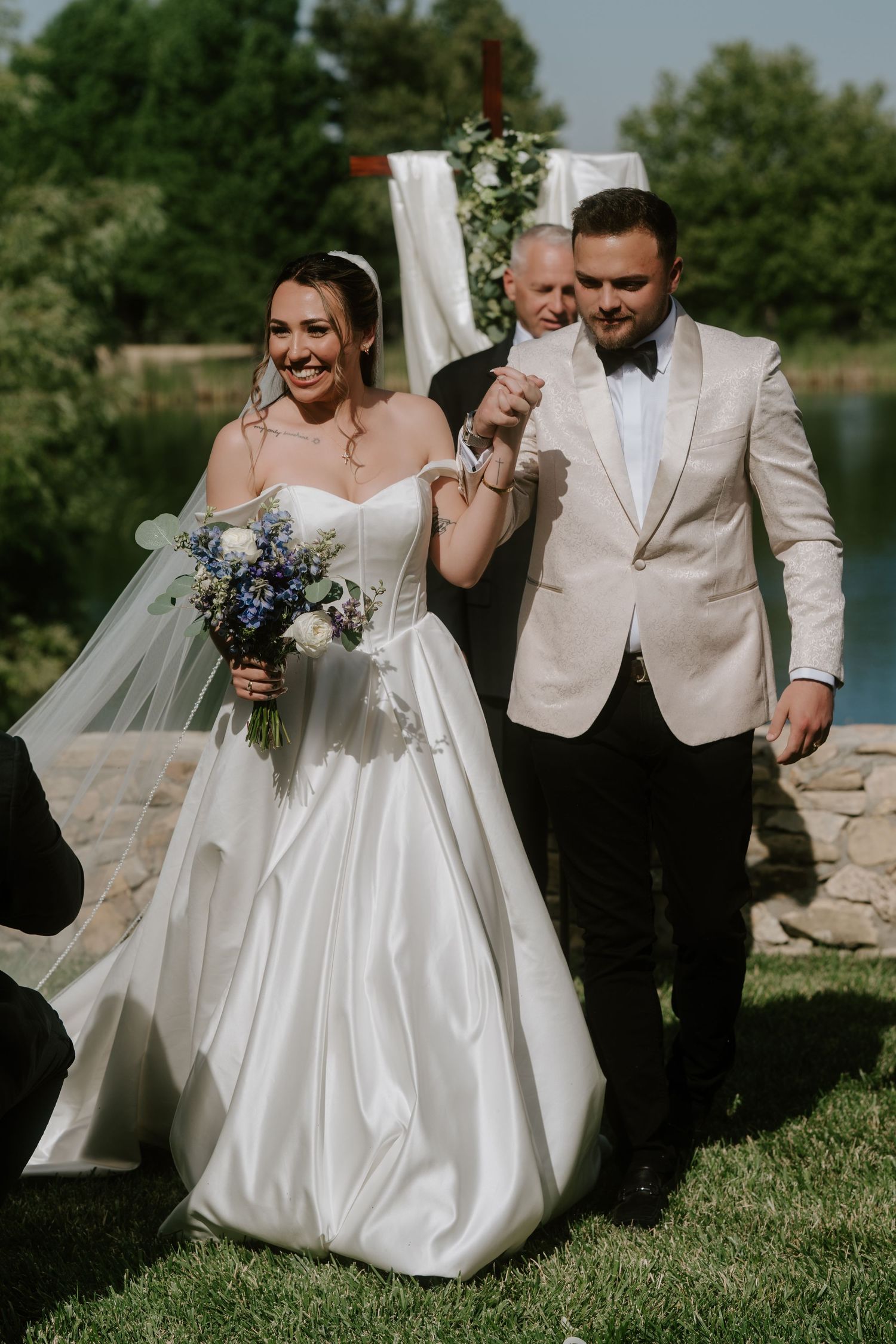 Bride and groom walk down the aisle after outdoor wedding ceremony, bride holds blue and white bouquet.
