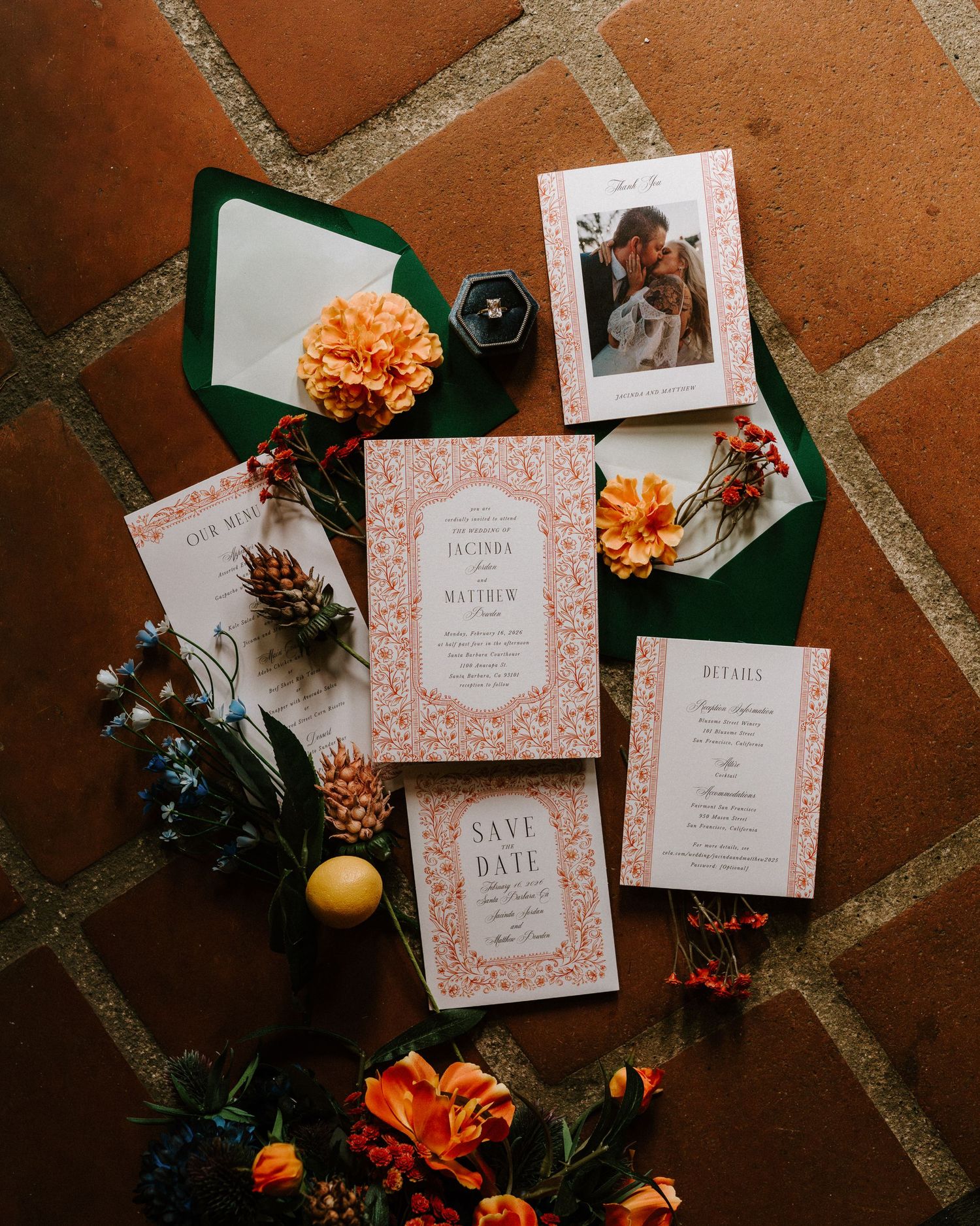 Wedding flatlay with pink floral invitations, save the date, and orange flowers on tile.