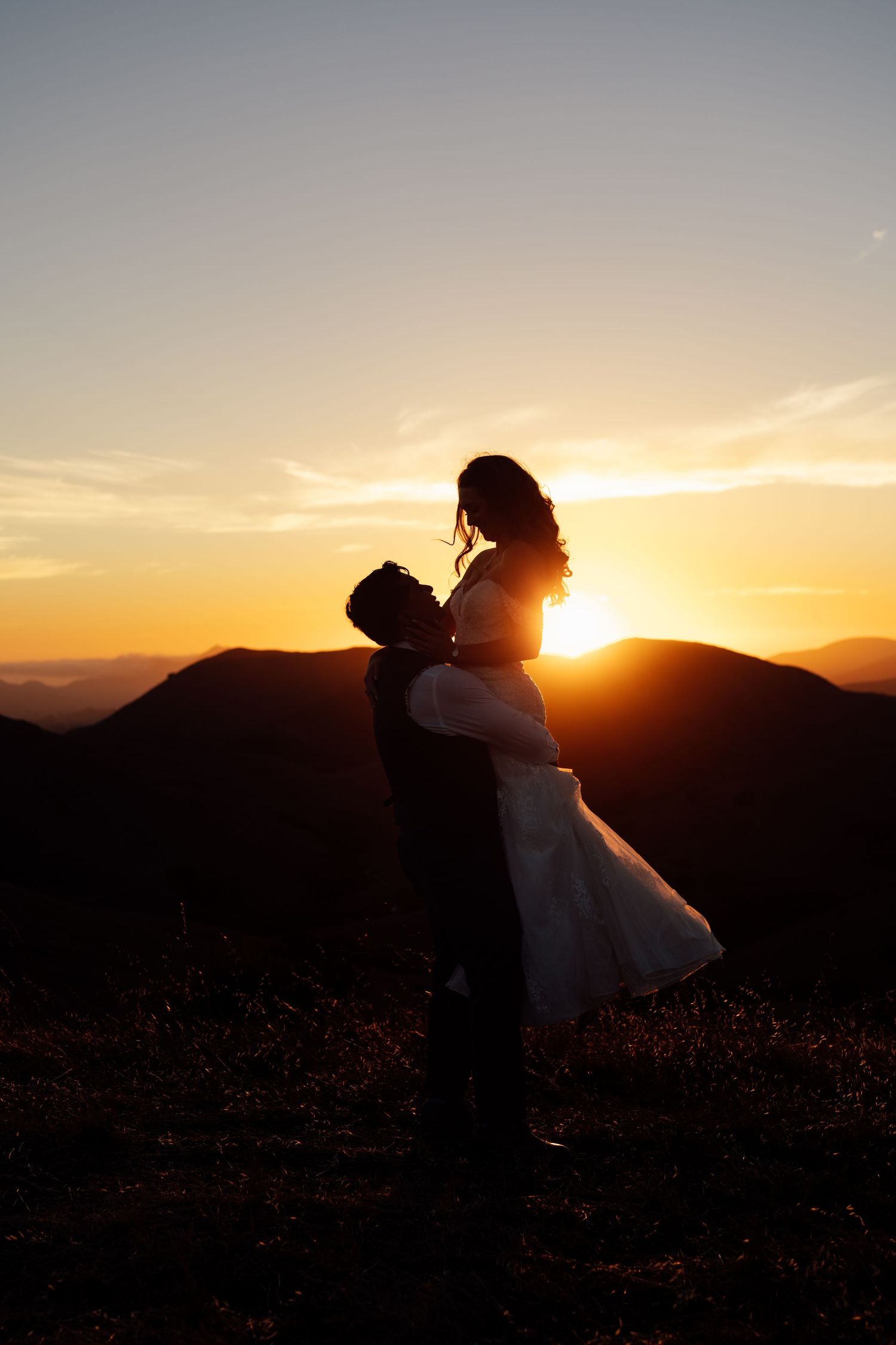 Silhouette of newlyweds embracing at sunset with mountains in the background, perfect for a romantic wedding photo.