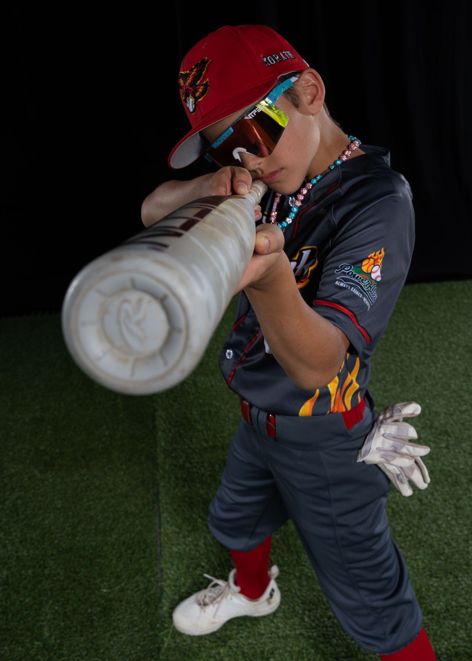 Young Firehawks baseball player in gray jersey swinging bat with batting gloves and red cap.