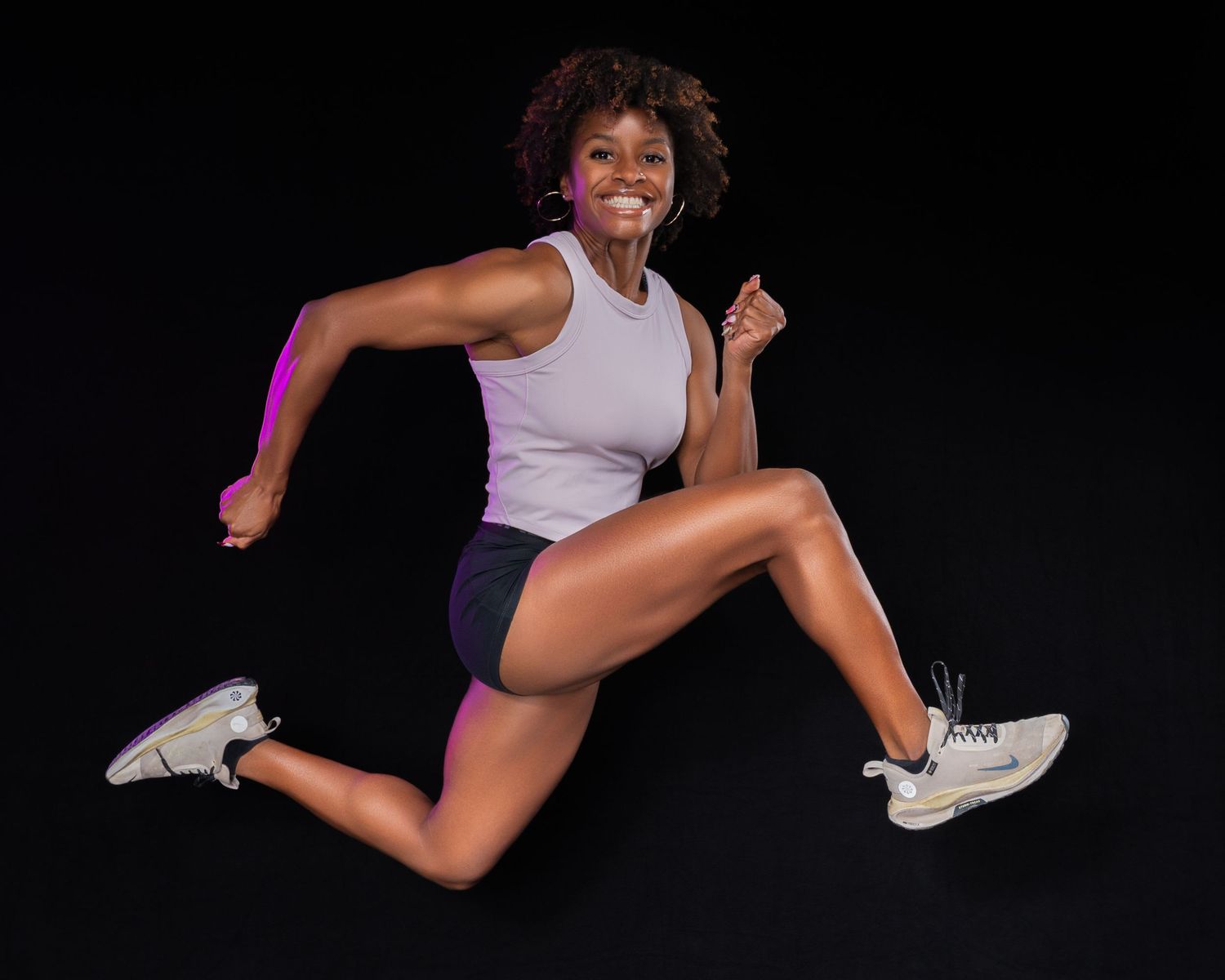 Athletic woman jumps energetically in sportswear against a dark background with purple lighting accent.