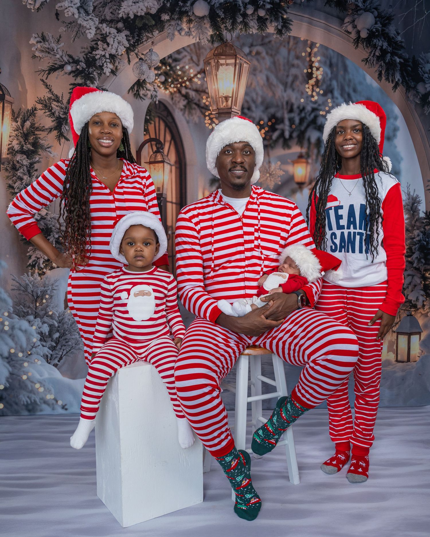 Family of four in matching red and white striped Christmas pajamas and Santa hats posing for a festive holiday photo.