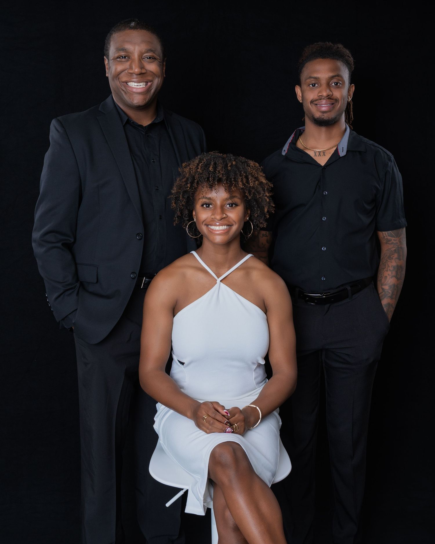 Family portrait of three people dressed in black and white against a dark background.