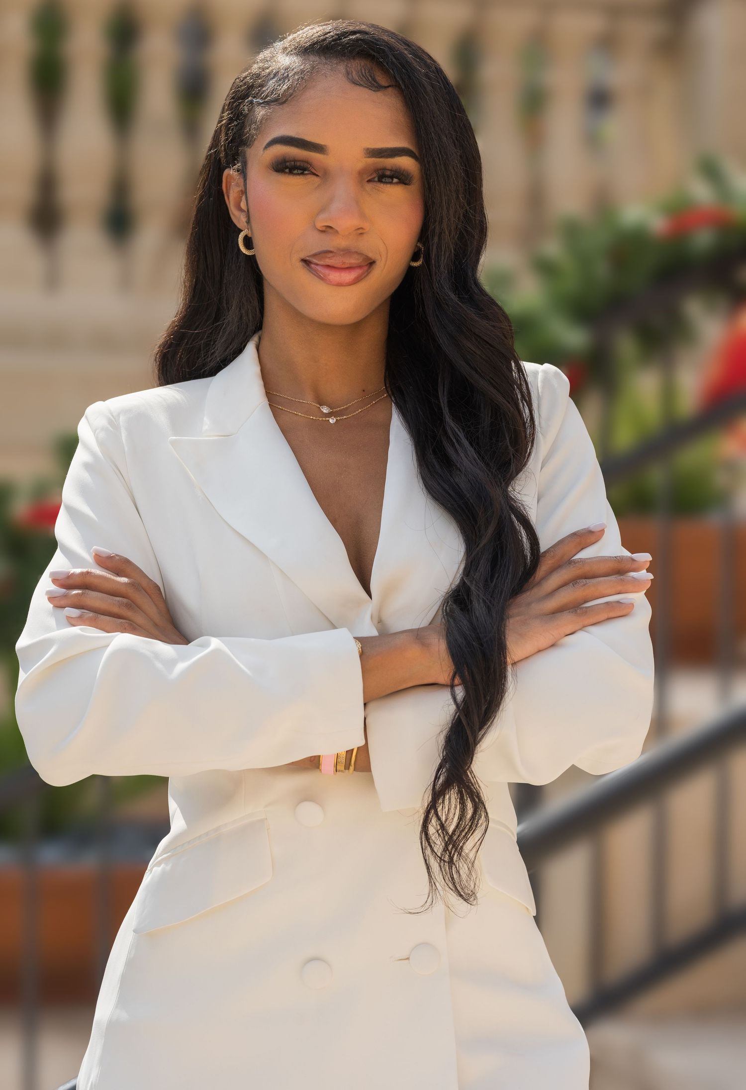 Confident young woman in white blazer suit with arms crossed posing outdoors in professional portrait.