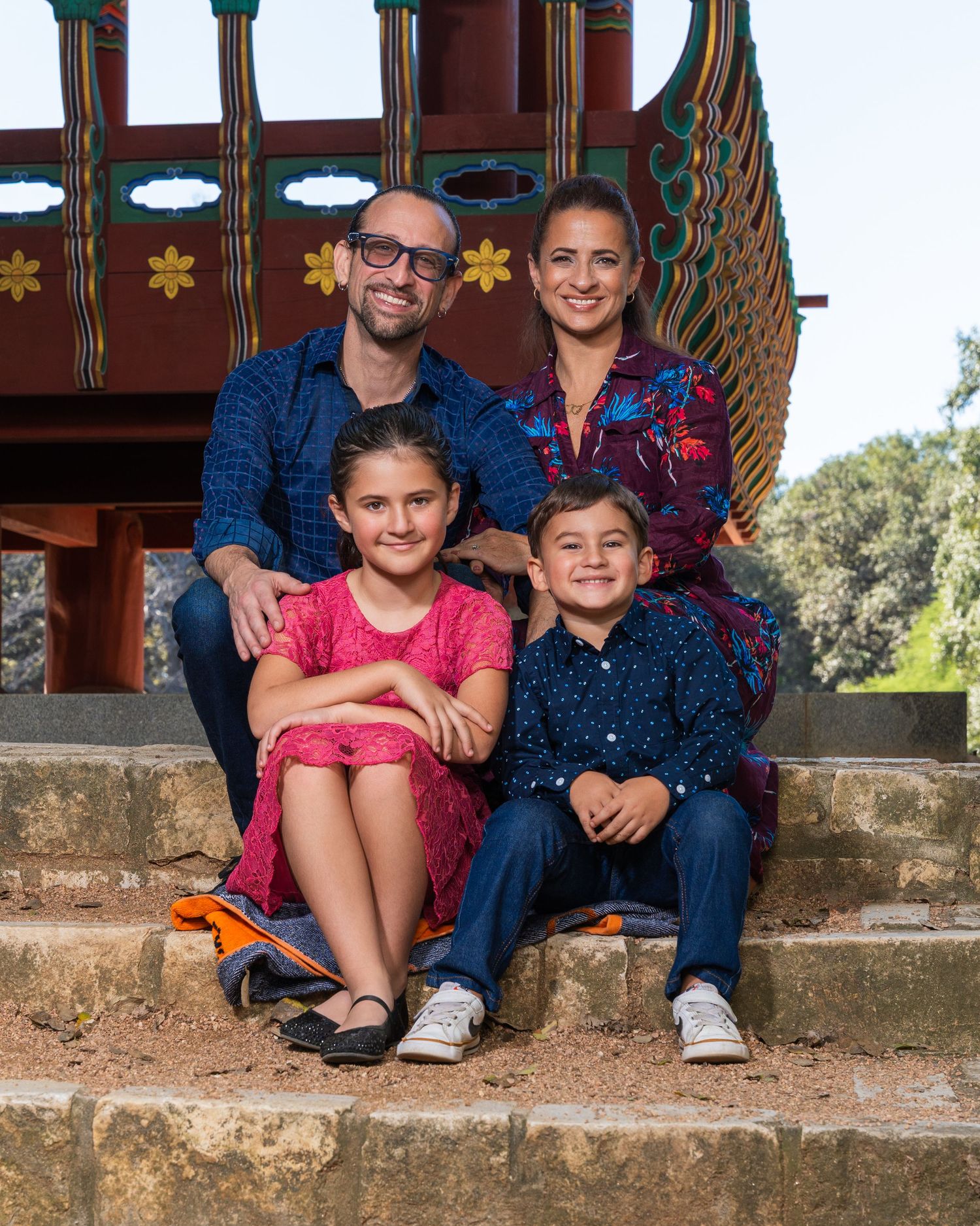 Happy family of four sitting on steps in front of a colorful decorative structure outdoors.