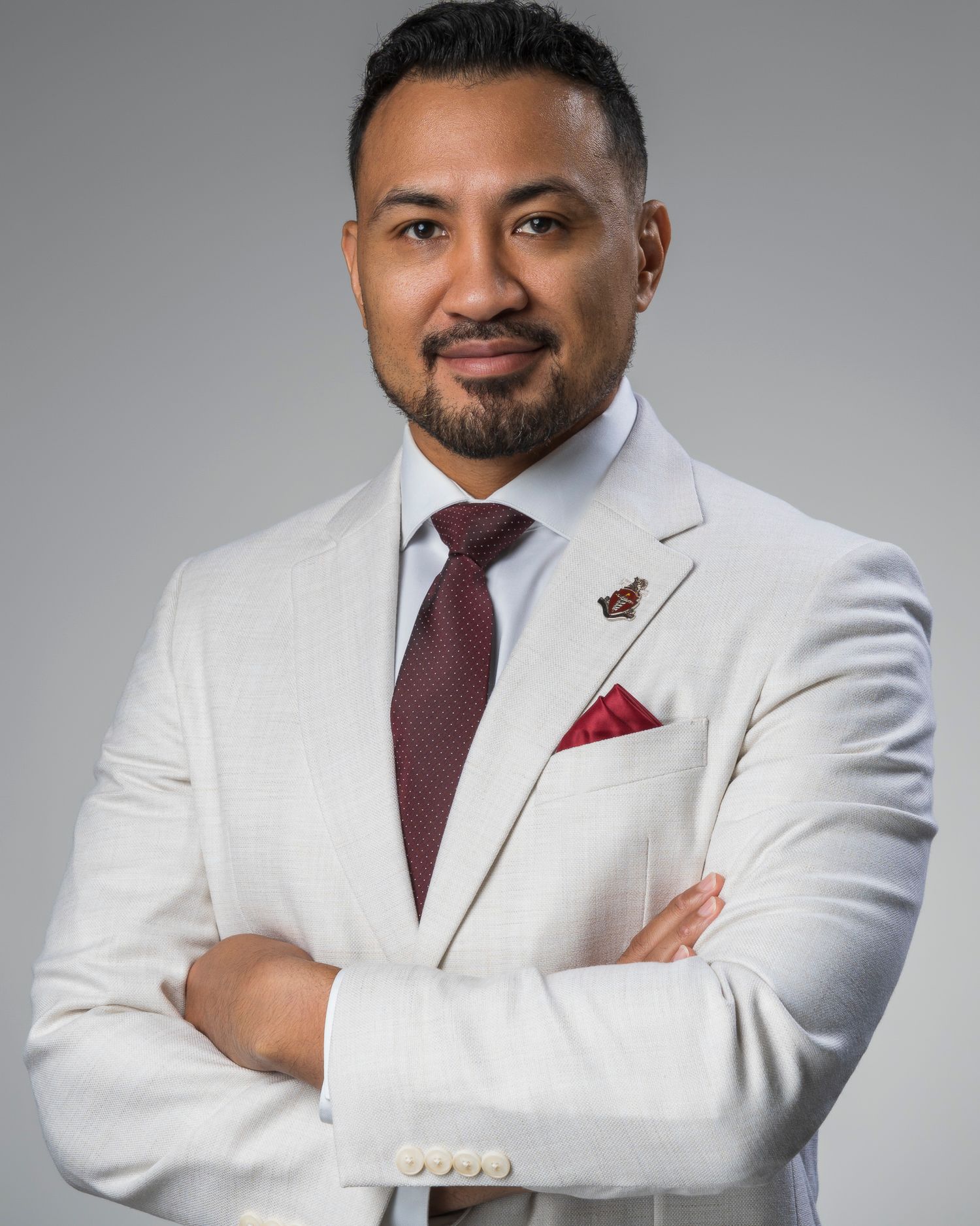 Professional man in white suit with red tie and pocket square, arms crossed, posing for a formal business portrait.