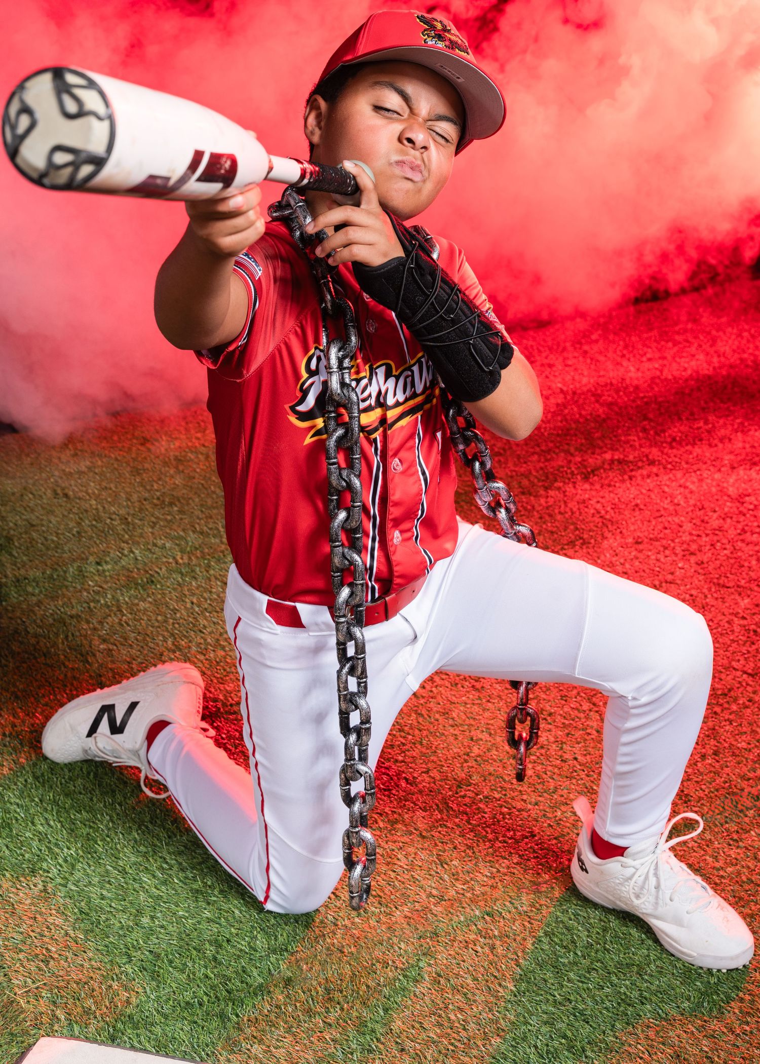 Young baseball player in red Firehawks uniform posing with bat and chains.