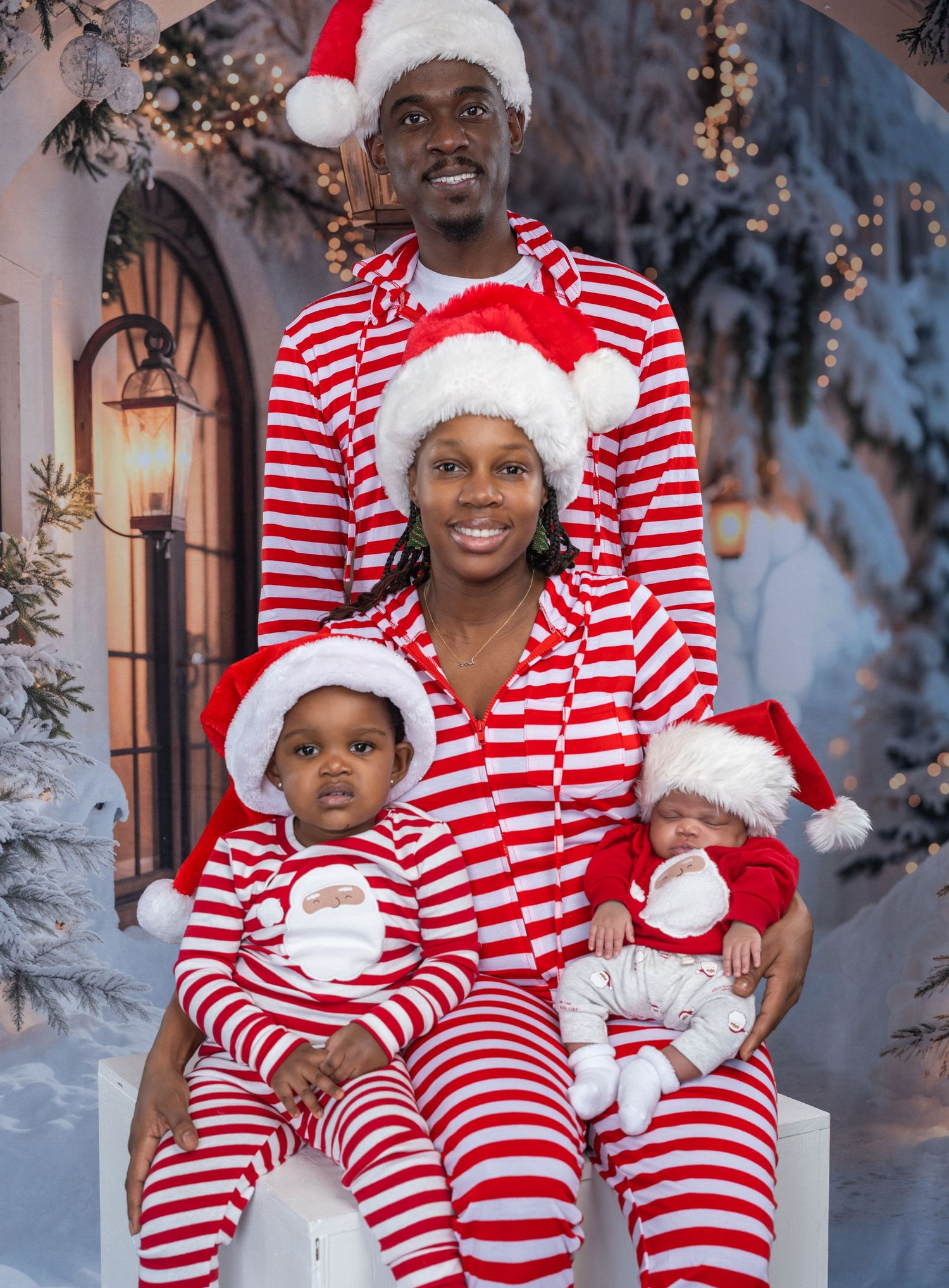 Family of four in matching red and white striped Christmas pajamas and Santa hats posing for a holiday photo.
