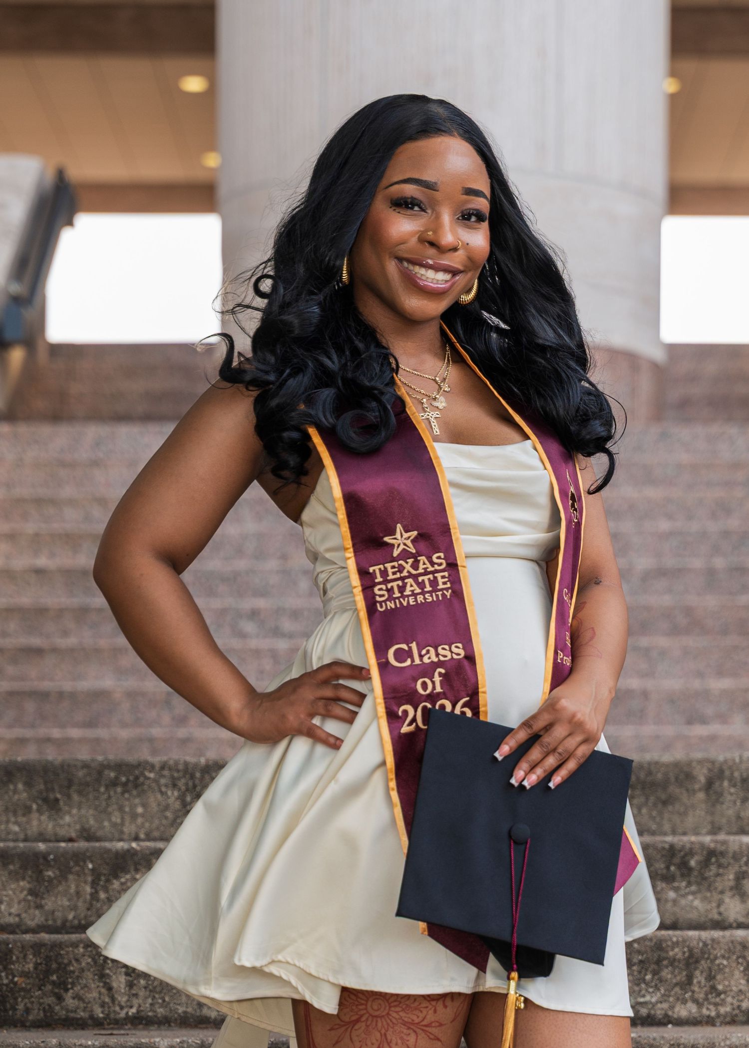 Texas State University graduate smiling in Class of 2026 maroon sash, holding cap on steps.