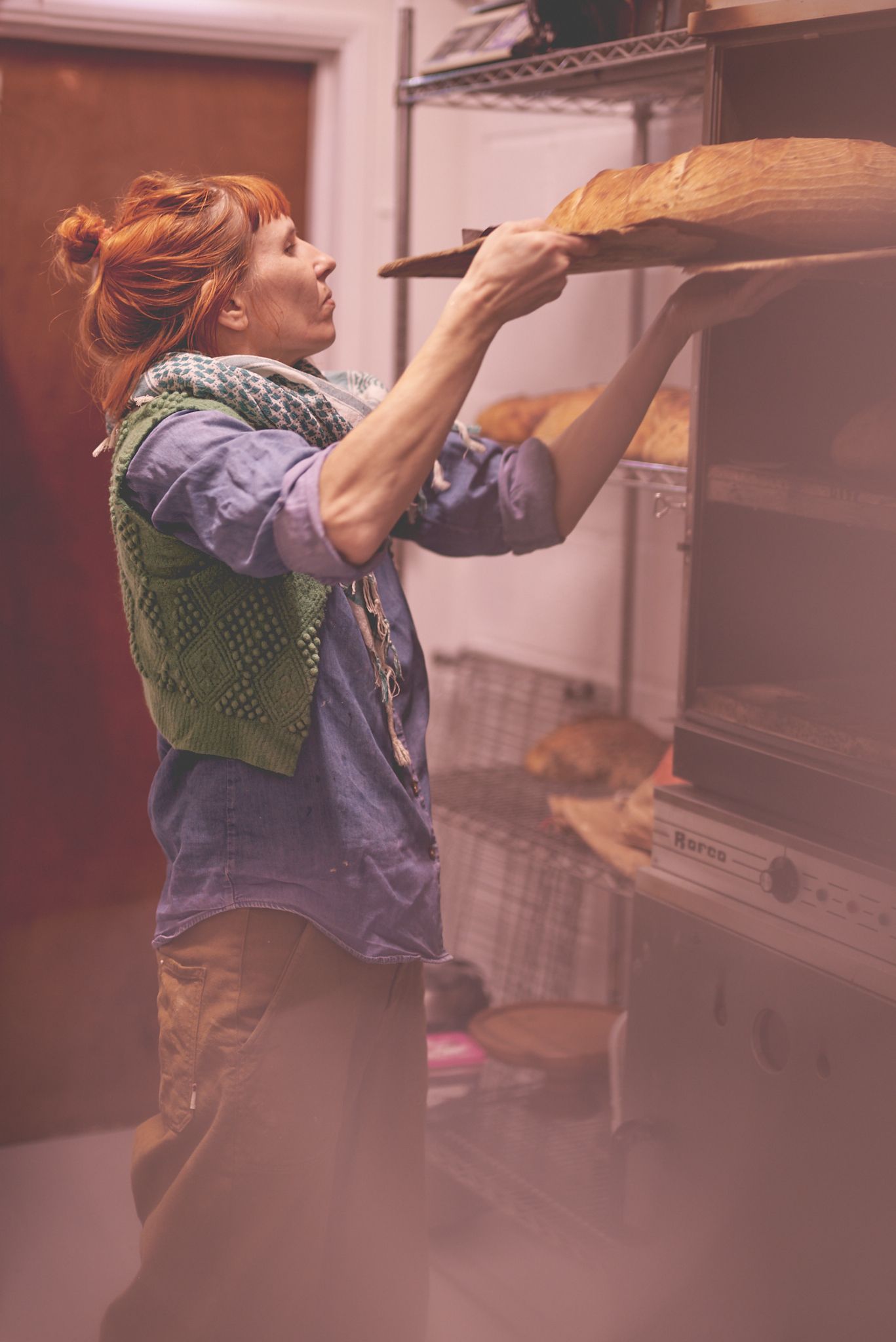 Female sourdough baker taking fresh bread out of the oven at New Street Market in Woodbridge