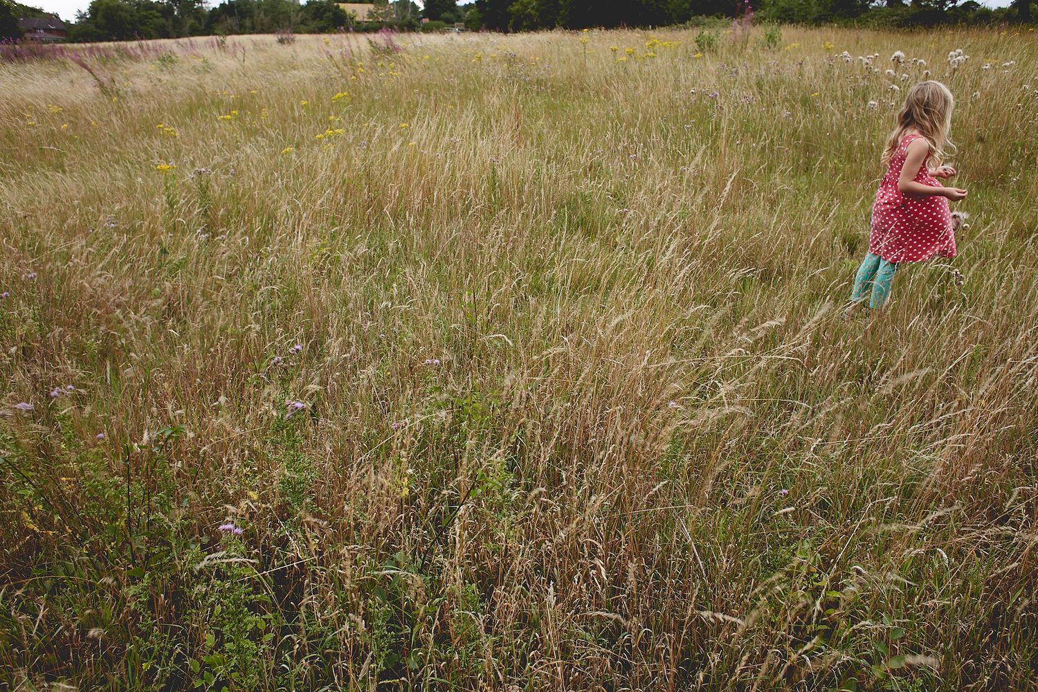 A girl in a grassy field with her back turned by Cat Heygate Photo