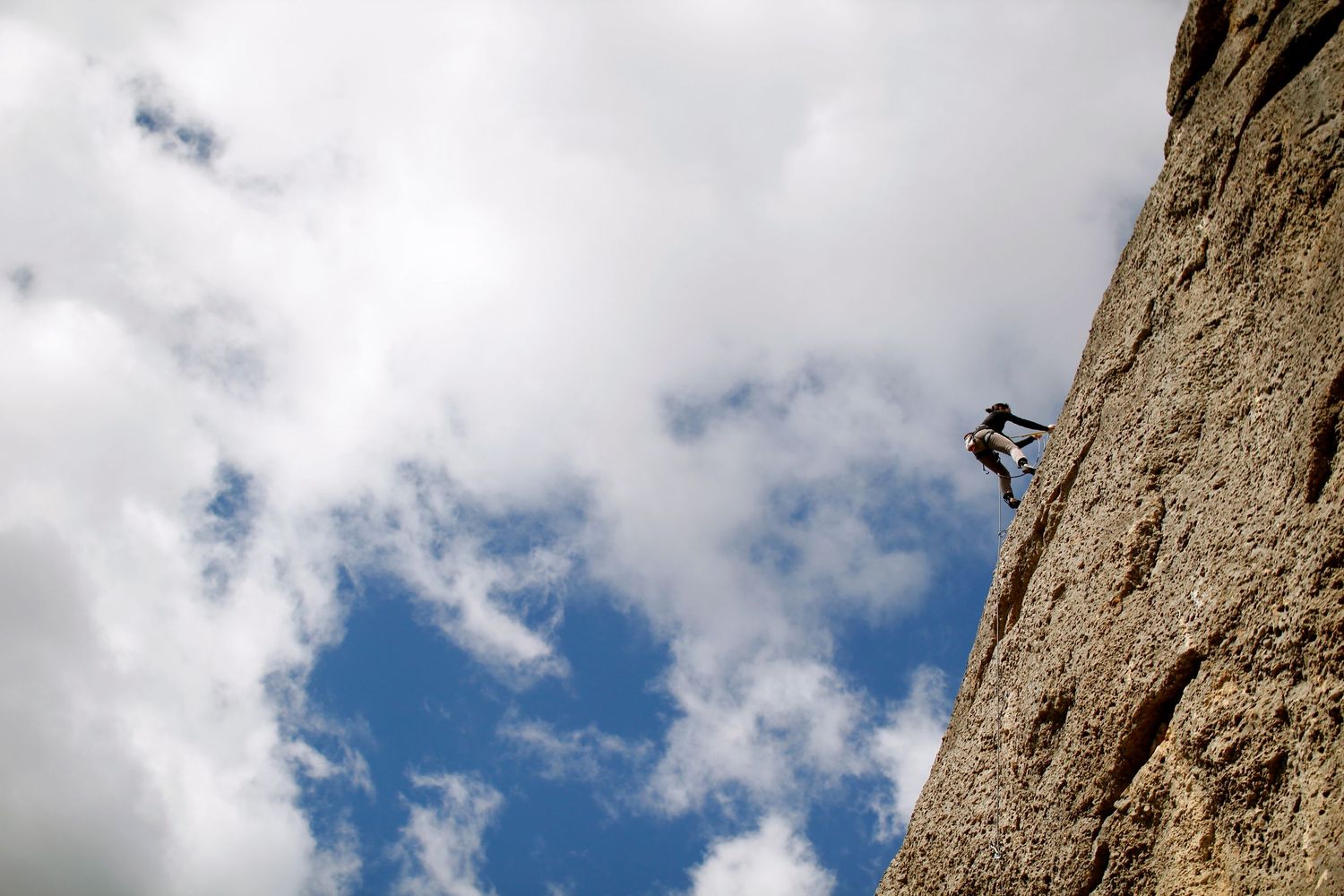 A woman rock climbing in Spain against clouds by Cat Heygate Photo