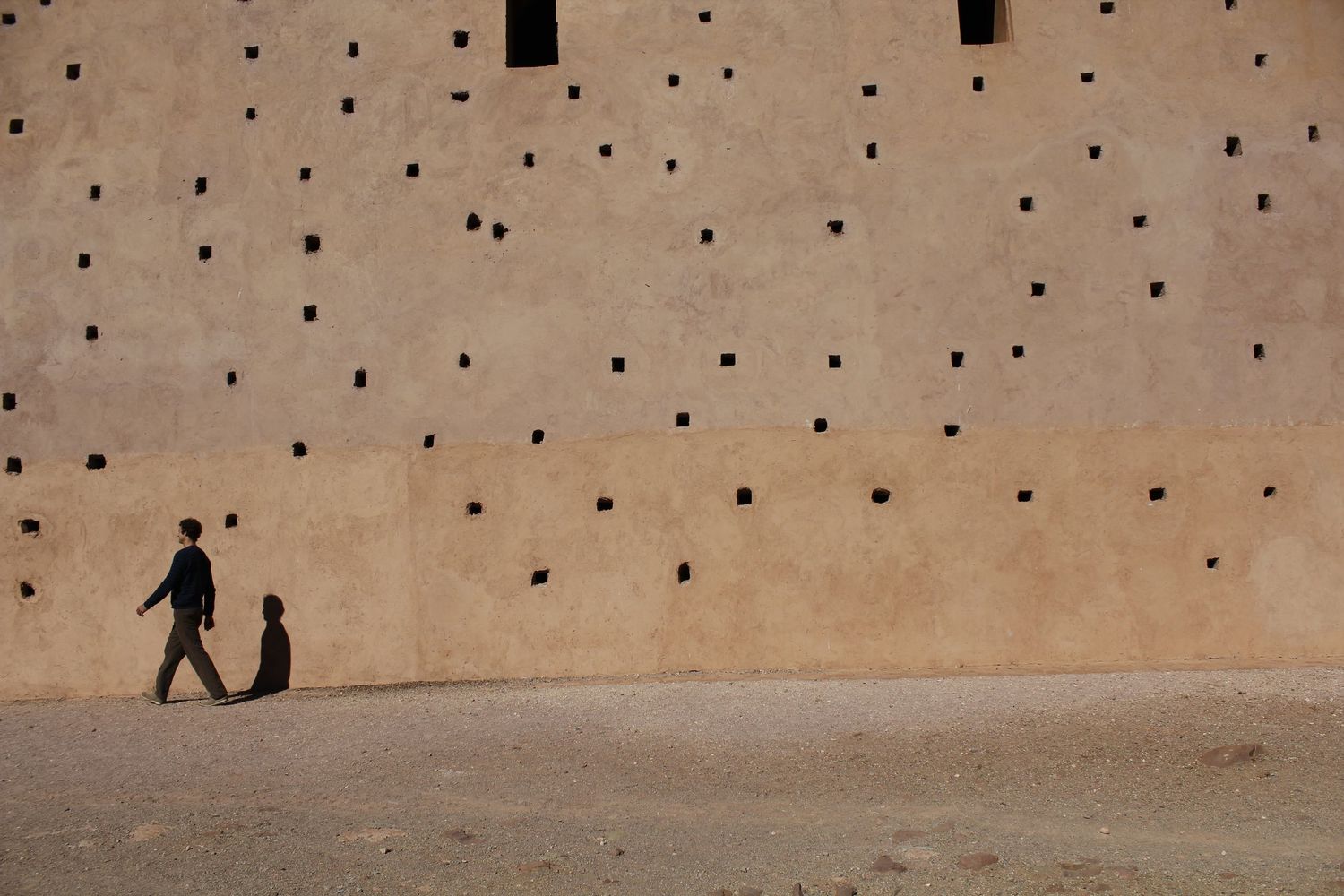 A man walking in front of wall in bright sunlight in the Atlas Mountains Morocco by Cat Heygate Photo