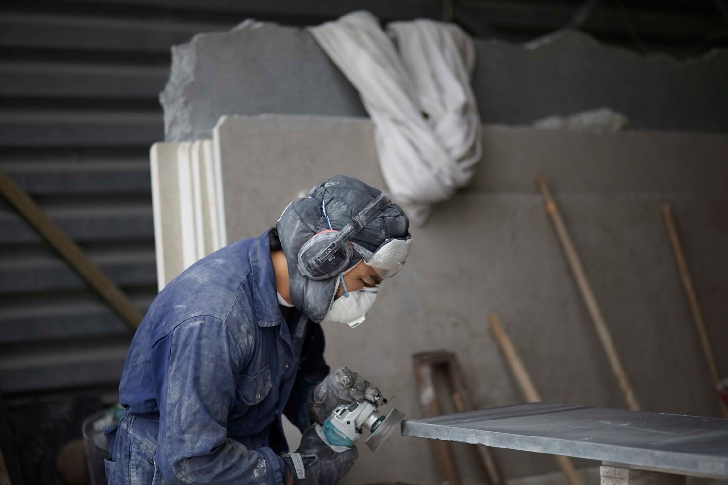Stonemason sanding edge of stone slab in his workshop for a small business photoshoot Woodbridge