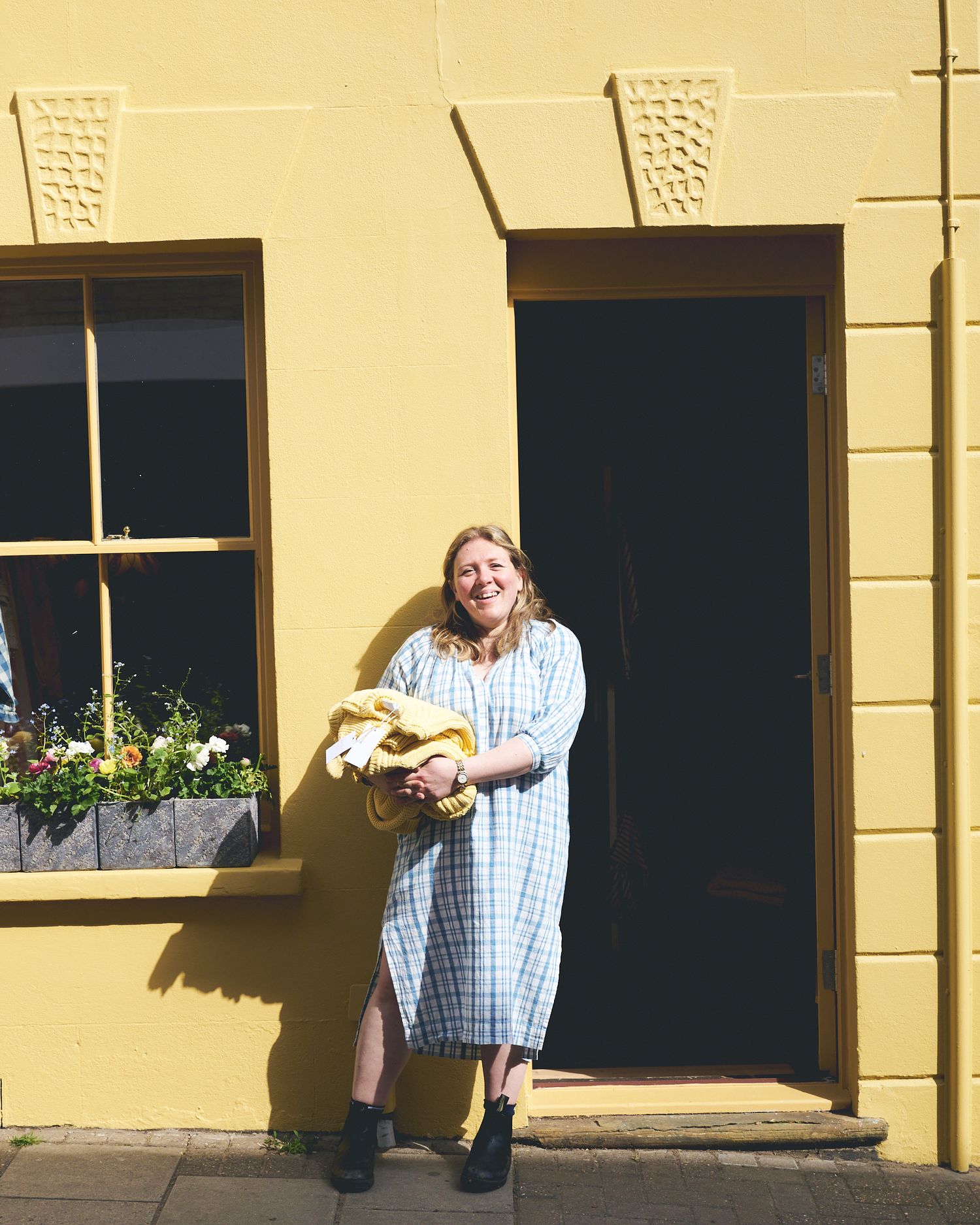 Female entrepeneur standing outside yellow shop in Woodbridge in bright sunlight smiling by Cat Heygate Photo
