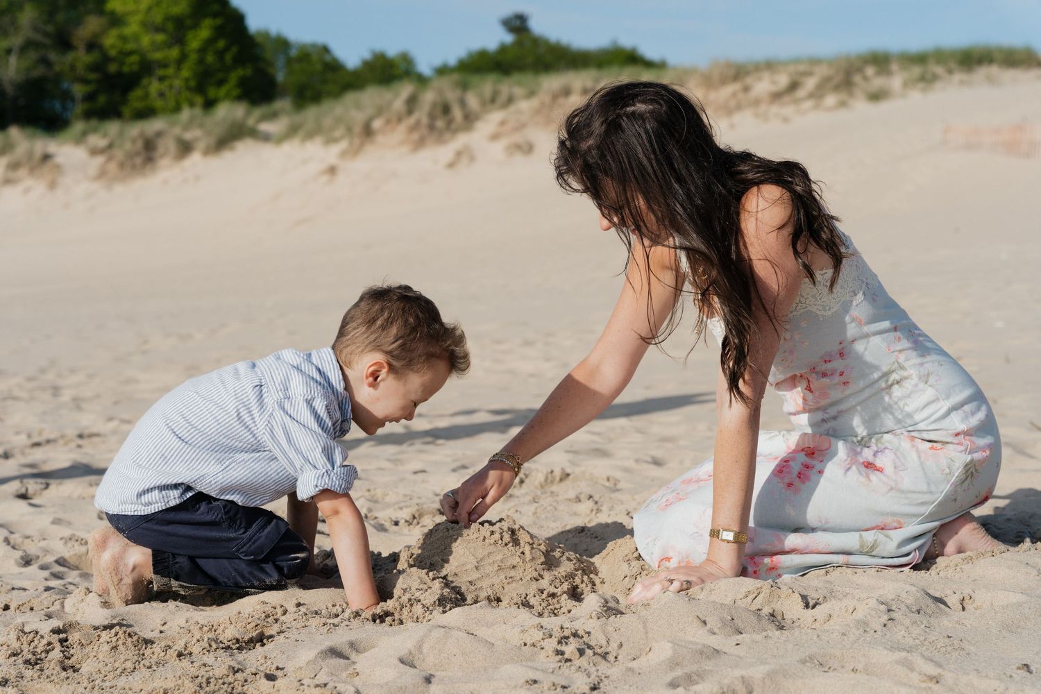 A mom and young boy playing together in the sand on a sunny beach day.