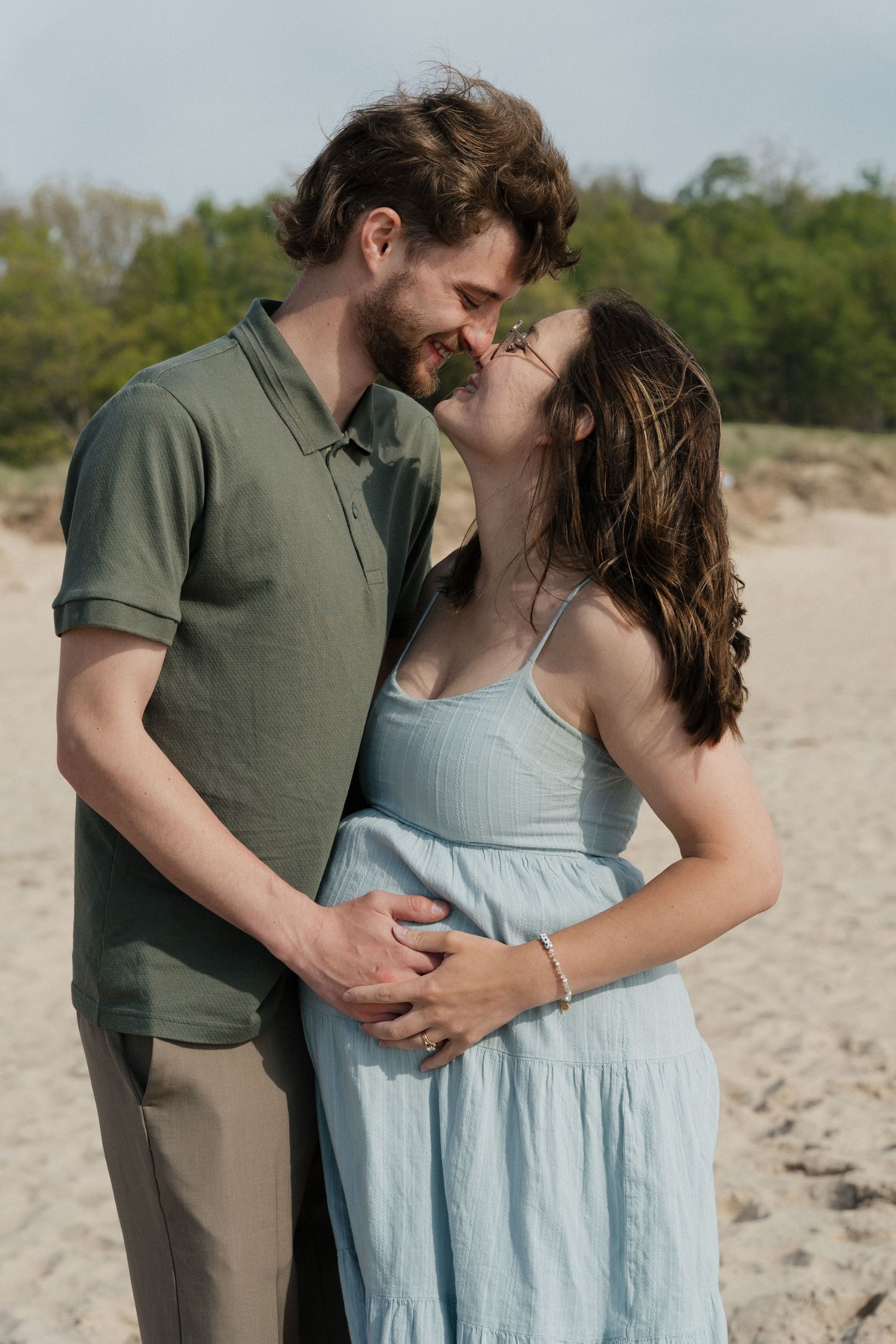 Couple sharing a romantic moment on a sandy beach, man in green shirt embracing woman in light blue sundress.