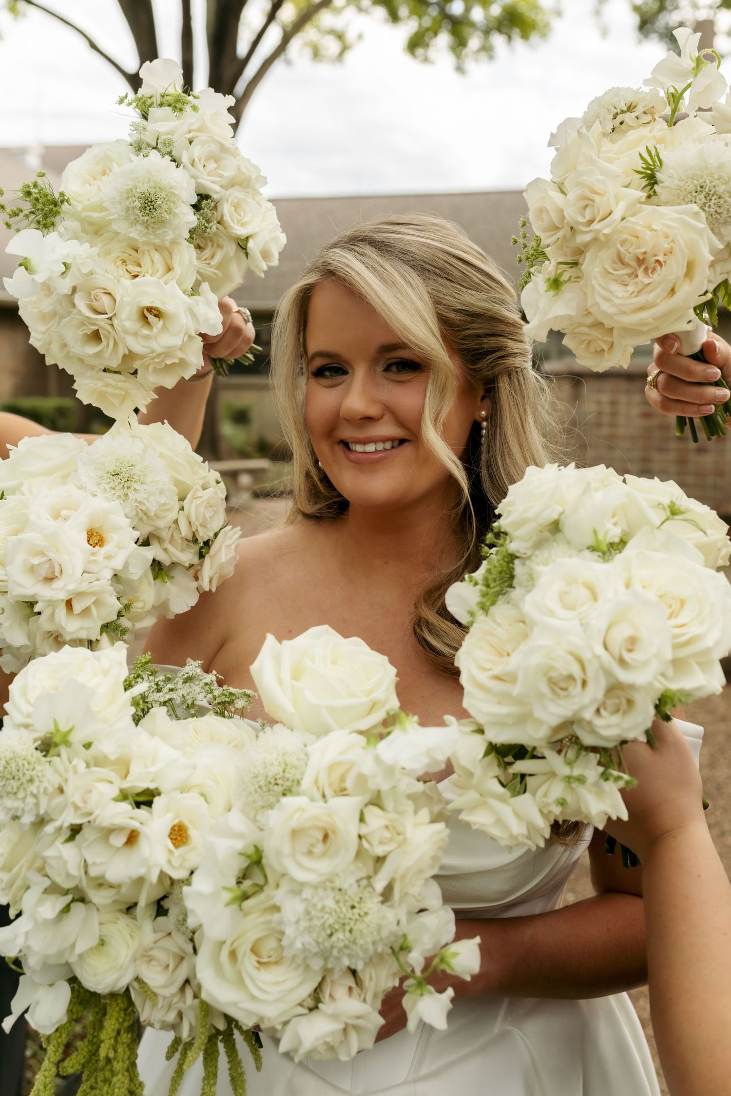 Smiling bride surrounded by multiple white rose and flower bouquets held by bridesmaids.