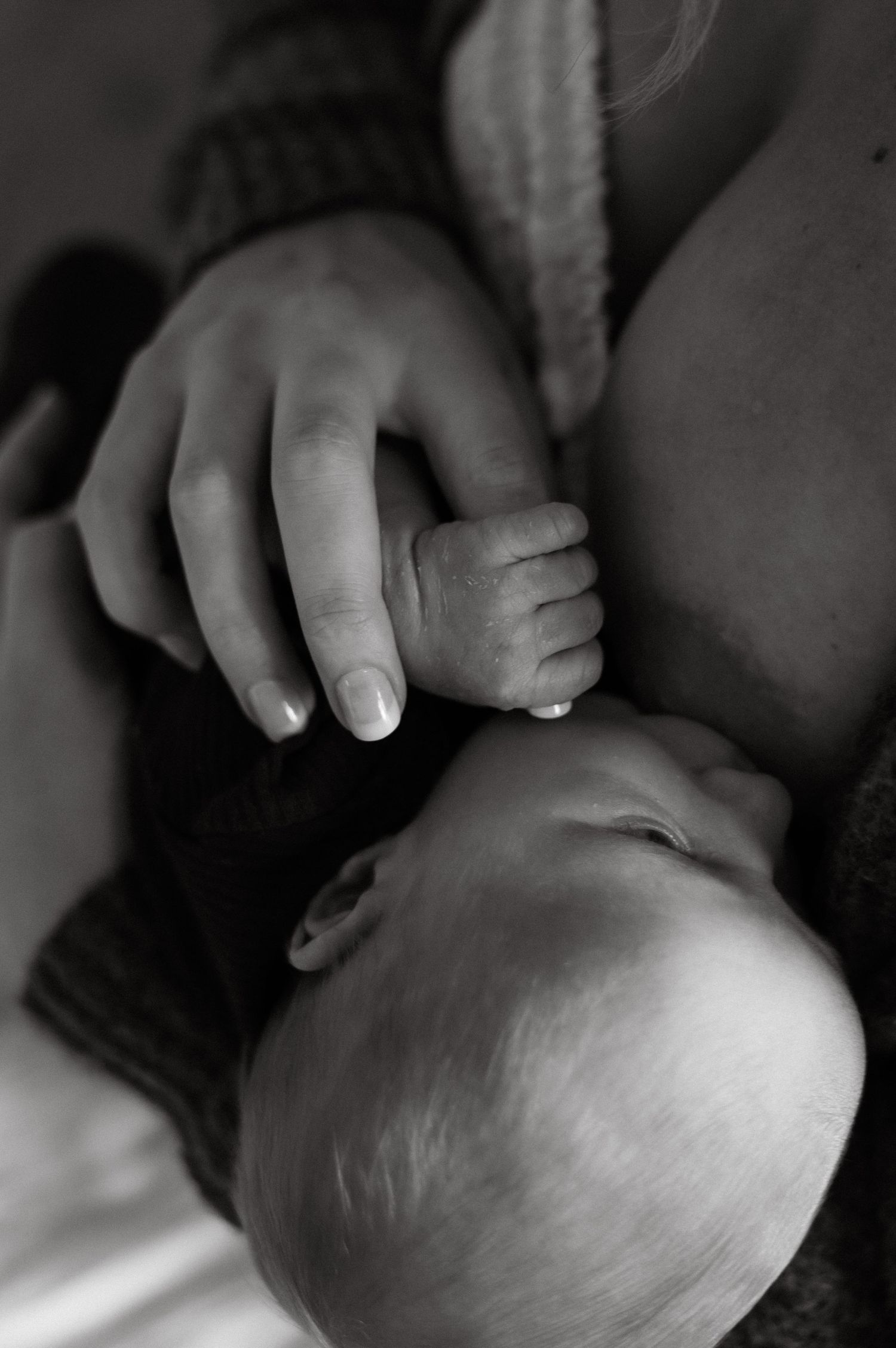 Black and white photo of a newborn baby holding a mothers finger while breastfeeding.